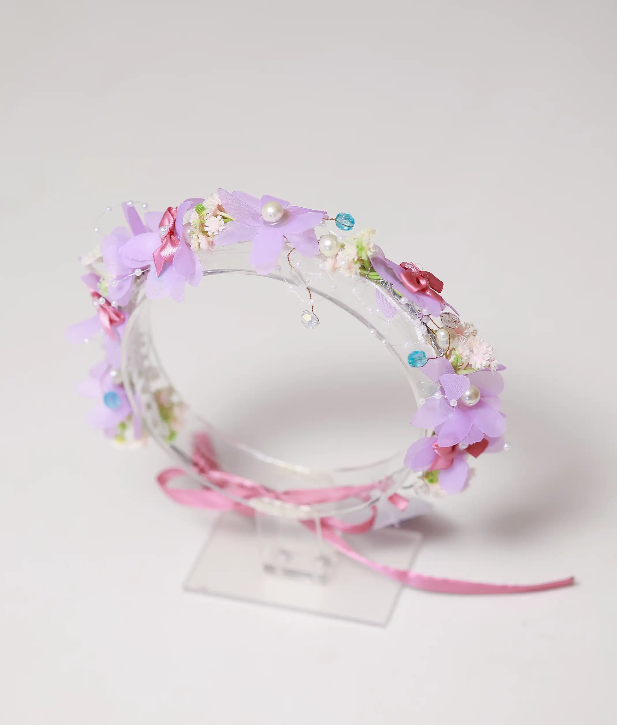 Close-up view of the handmade tiara showing lavender fabric flowers, white pearls, and pink satin bows