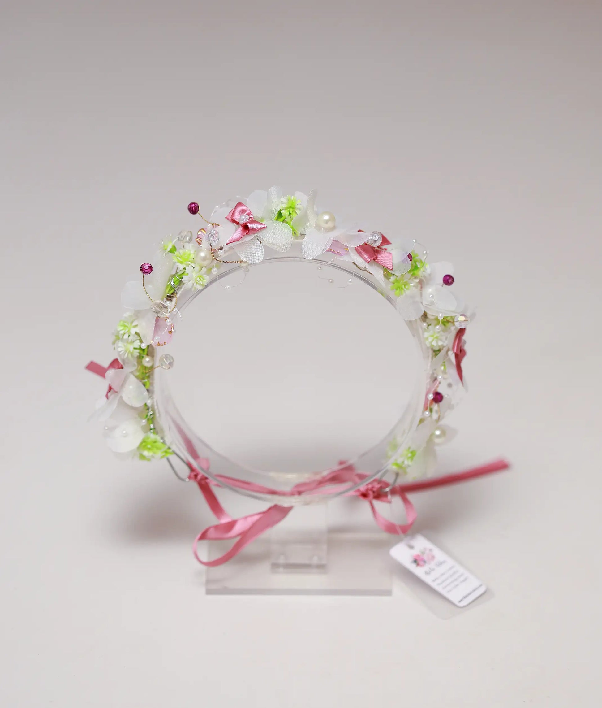 Close-up of the handmade tiara showing white fabric flowers, pink satin bows, pearls, and crystal accents