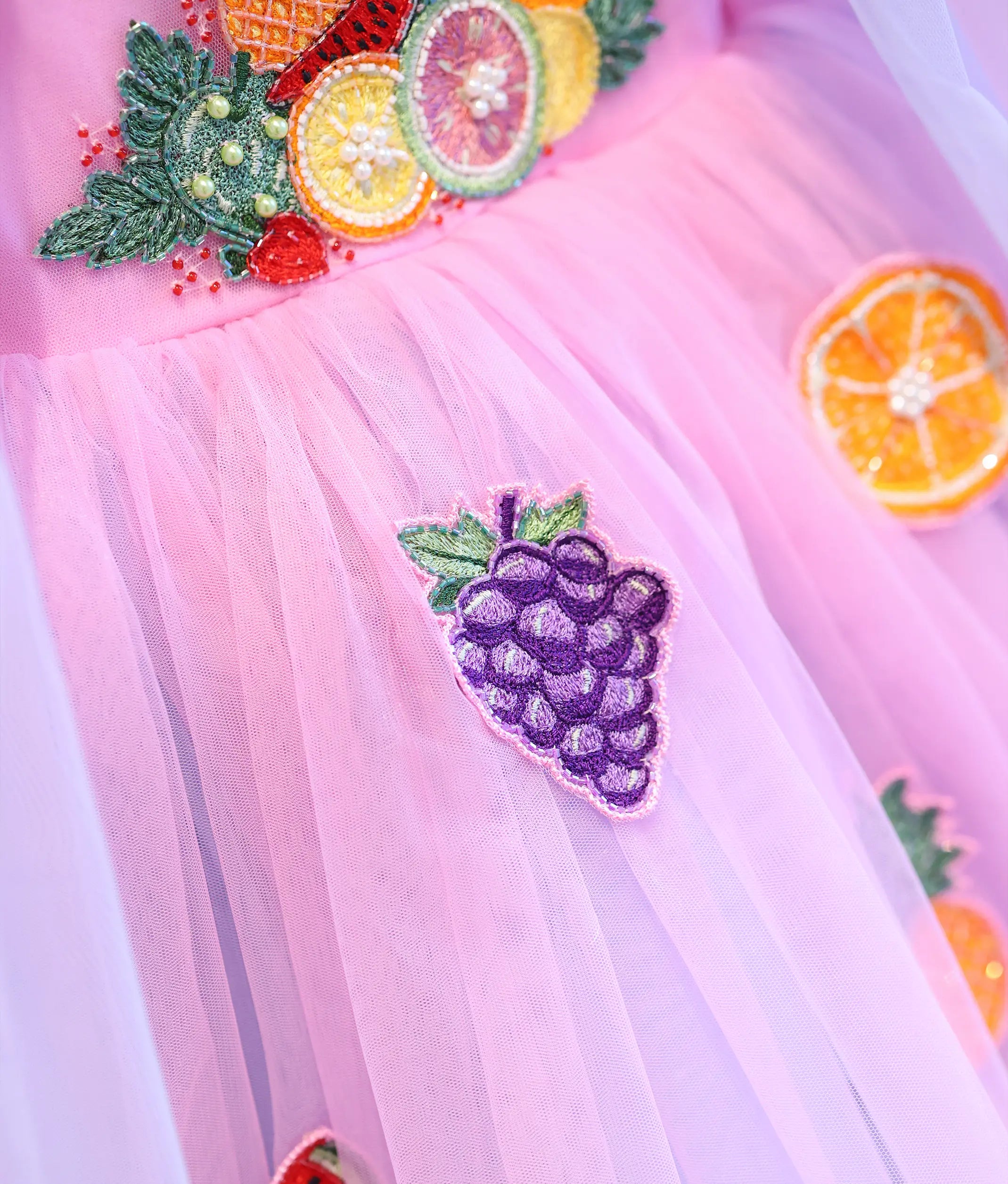 Close-up of pink and purple tulle party dress featuring grape, orange and handcrafted fruit appliqué embroidery on layered skirt