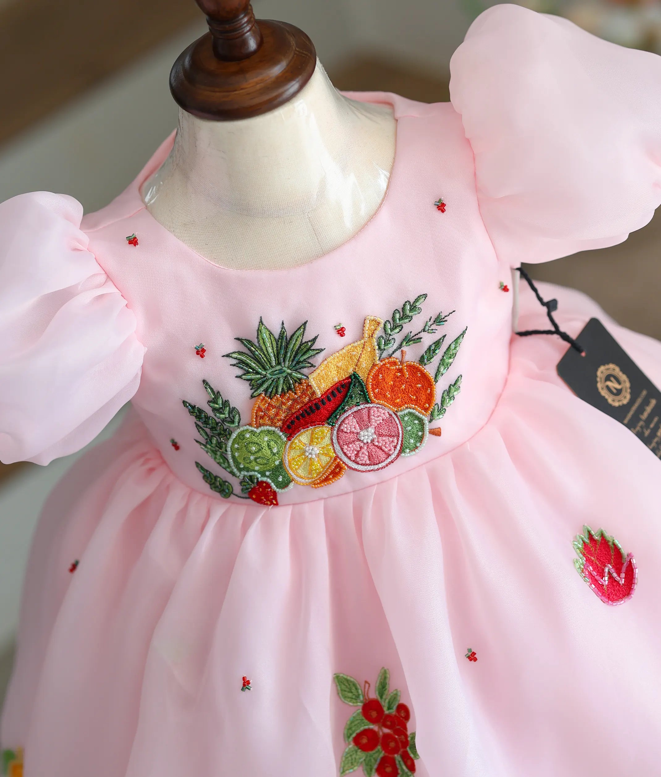 Close-up of the strawberry and floral handwork made with beads and threads on the pink bodice.