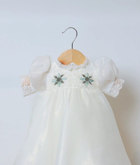 Close view of an plain organza fabric, showing the handworked floral yoke and delicate puff sleeves with lace.