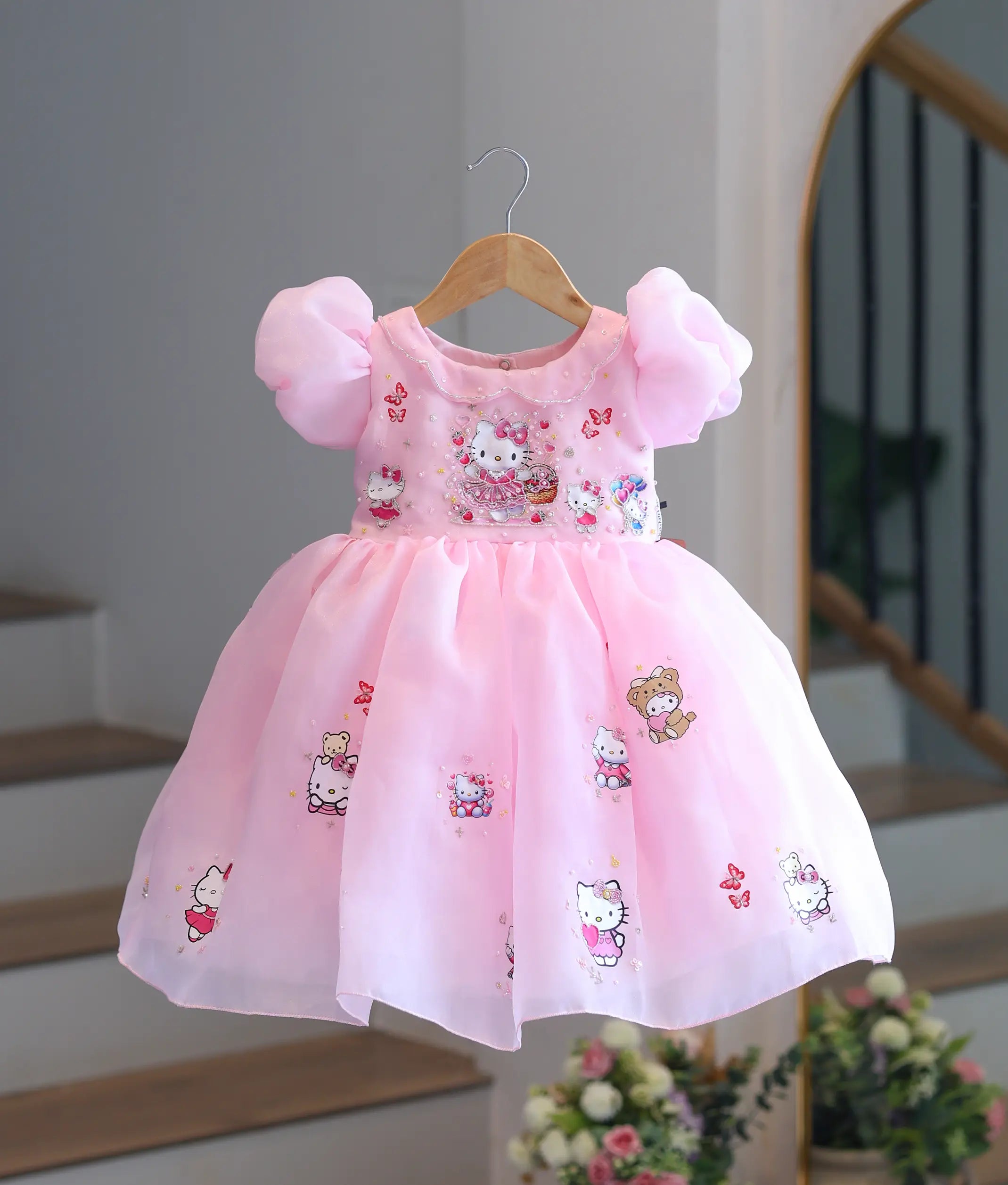Front view of baby pink shimmer organza Hello Kitty theme frock on hanger display.