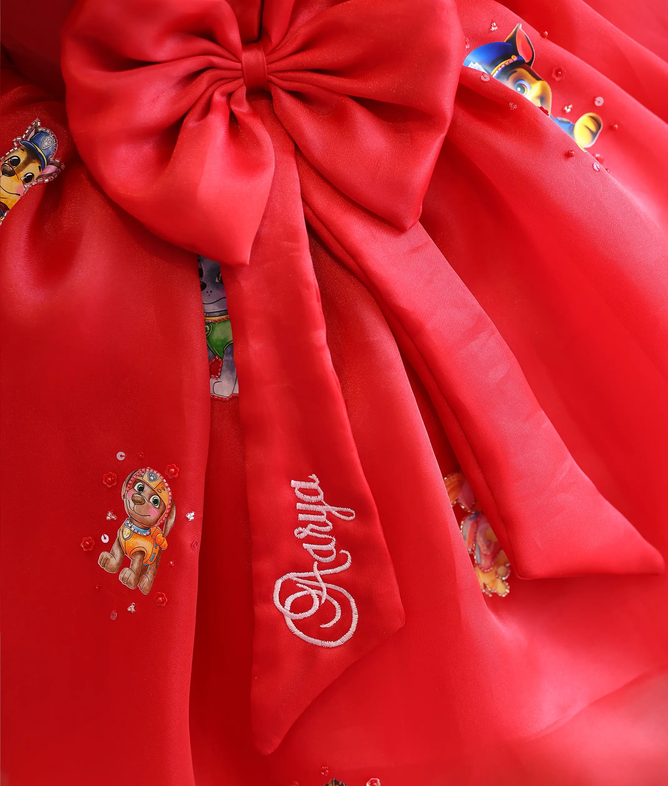 Close-up view of the big red organza bow featuring personalized name embroidery on the bow tail.