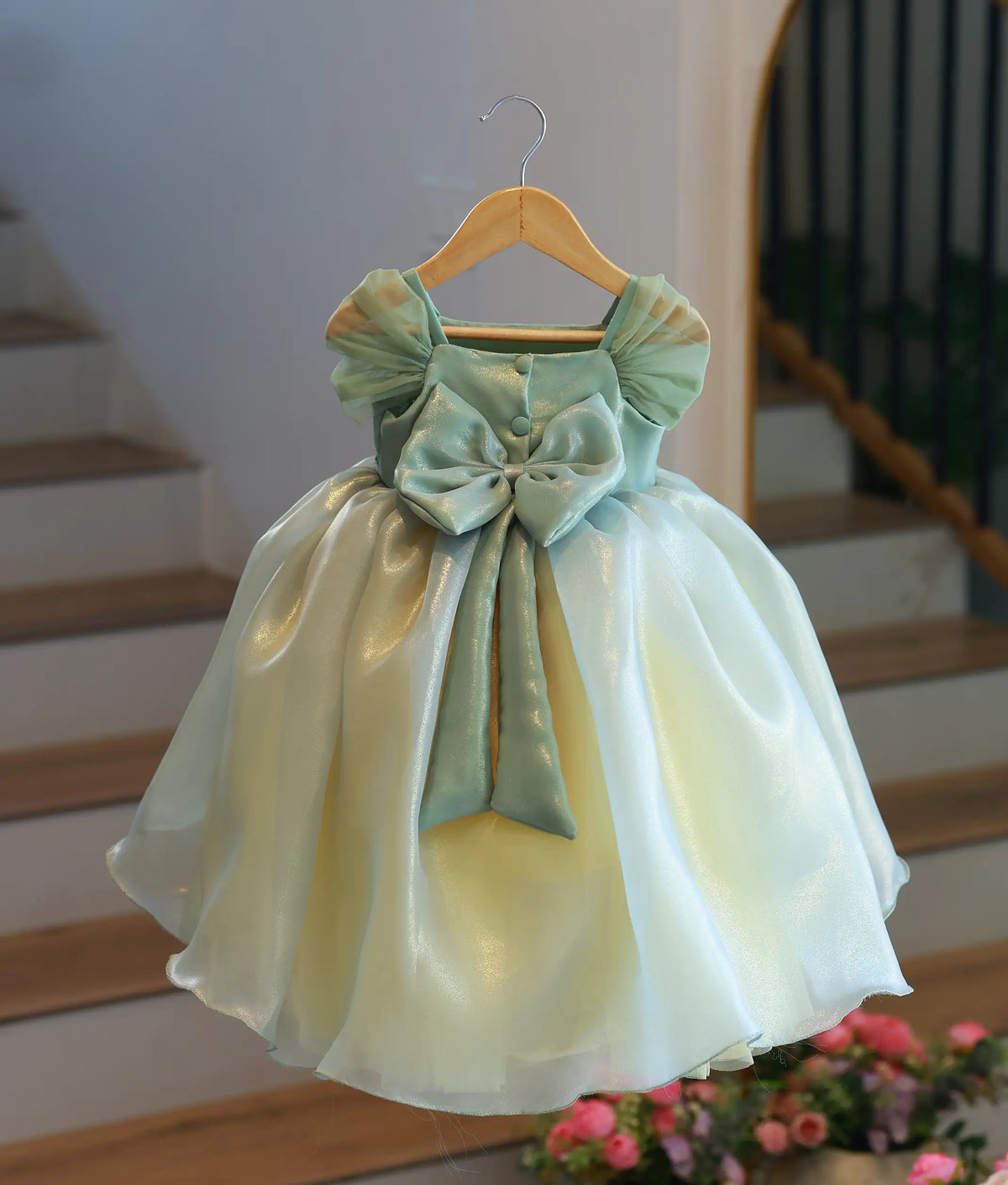 Back view of sage green organza frock showcasing large back bow and ruched sleeve details.