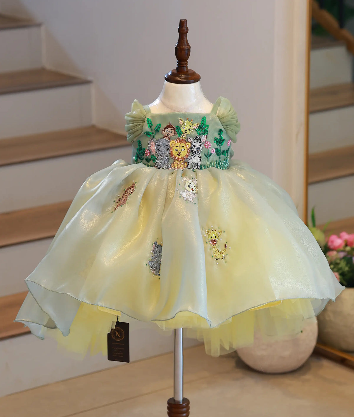 Front view of girls sage green organza jungle theme party frock with a high-low skirt and animal embroidery on mannequin.