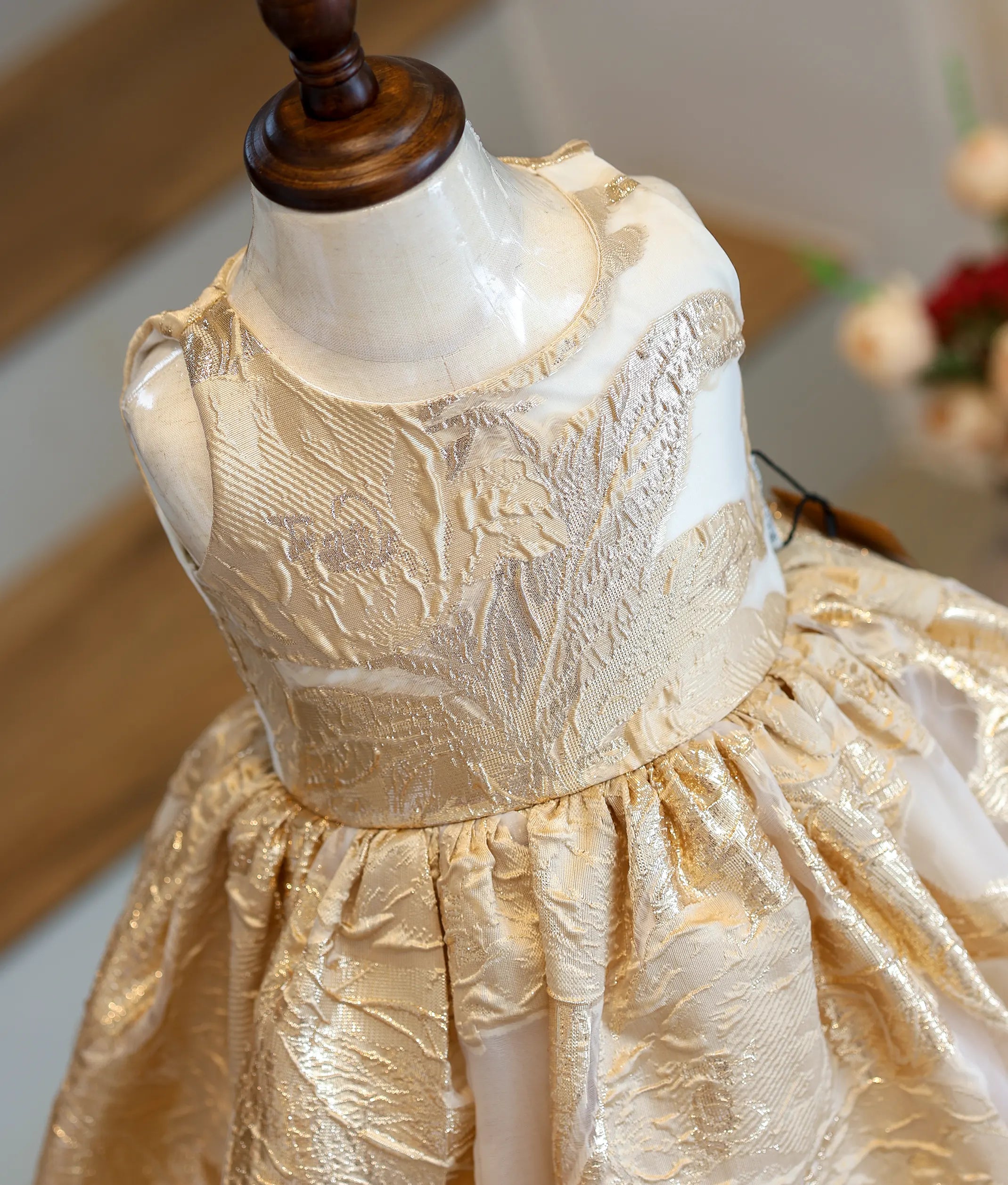 Close-up of the rich gold-toned floral pattern and round neck on the organza frock.