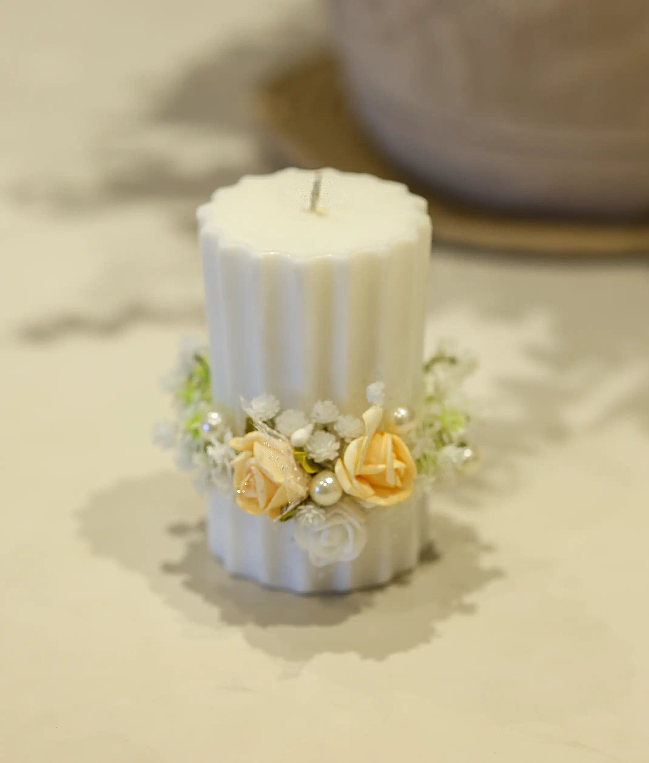 Close-up of a baptism candle featuring peach and white floral elements with off-white accents and pearls.