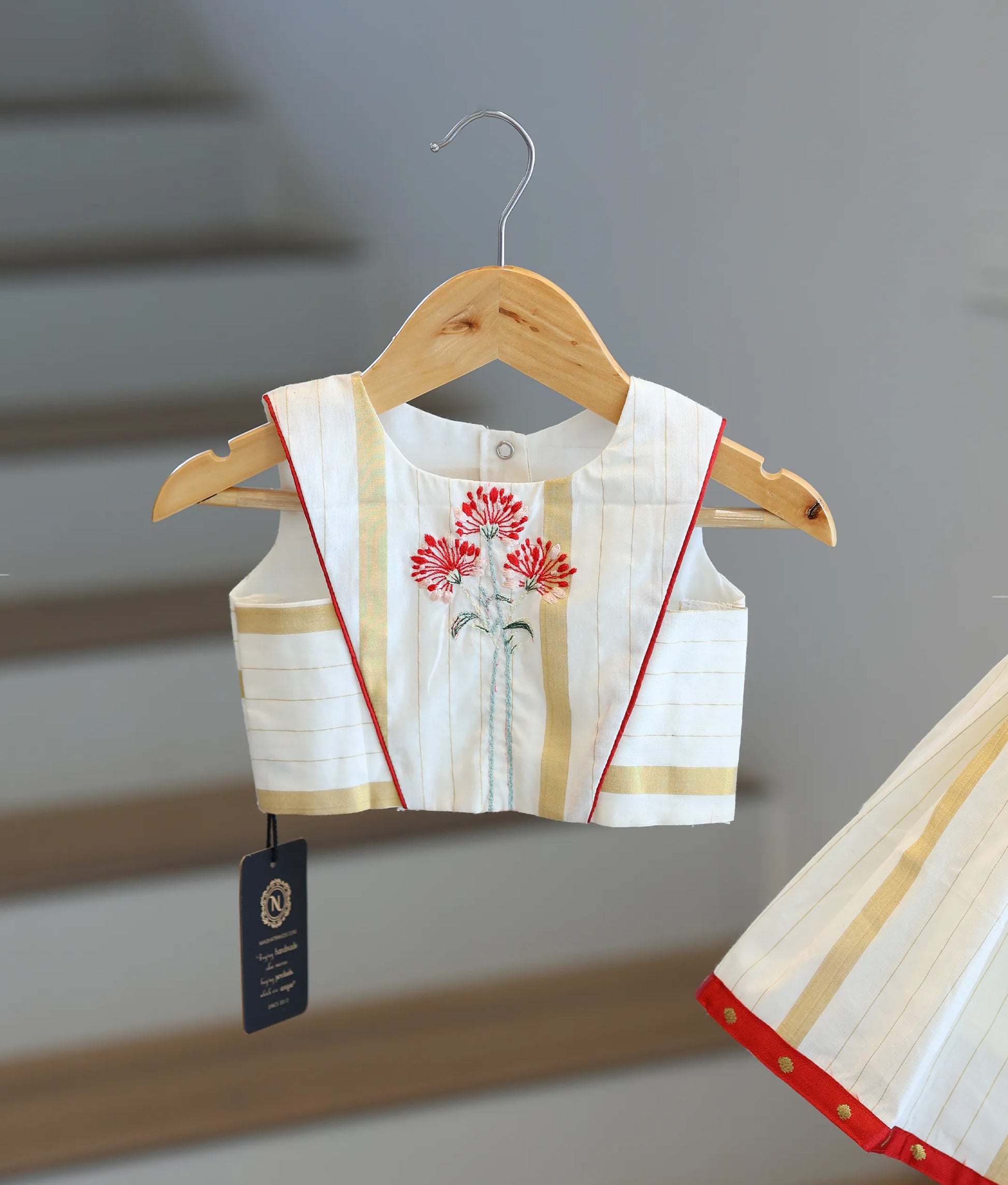 Close-up of the red floral embroidery and golden stripe patterns on the Kasavu skirt and top.