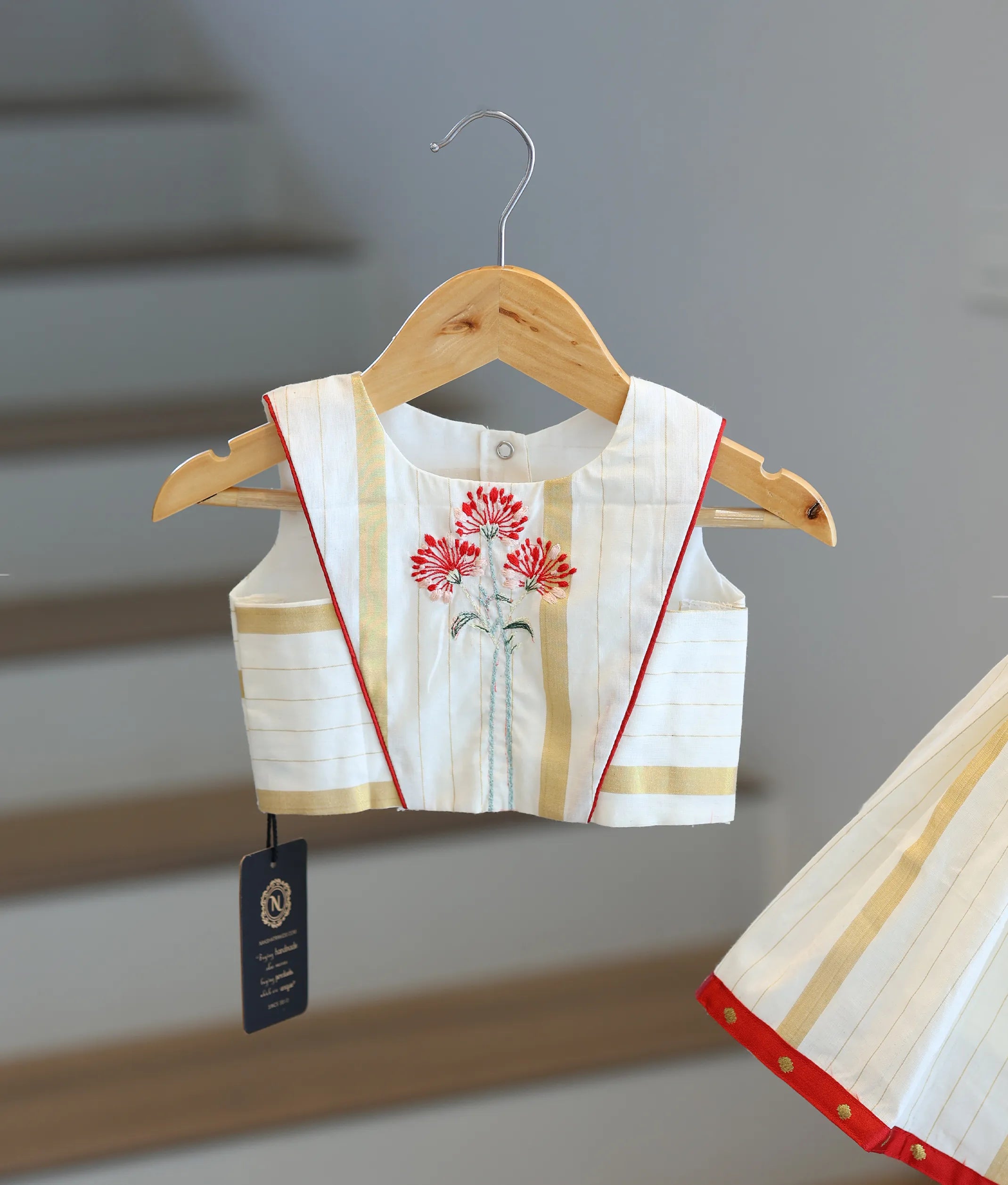 Close-up of the red floral embroidery and golden stripe patterns on the Kasavu skirt and top.