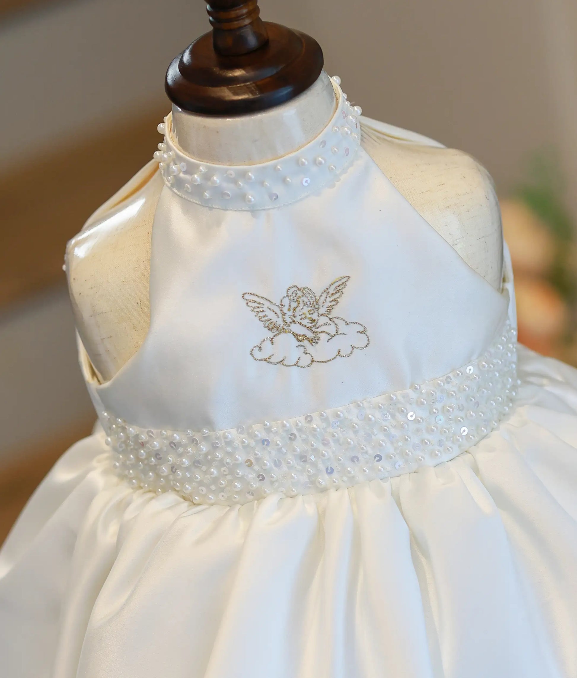 Detailed close-up view of the gown top, highlighting the gold-embroidered angel on a cloud, pearl-beaded collar, and matching wide pearl waistband.