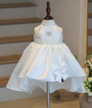Full front view of a premium kid's off-white satin high-low baptism frock on a mannequin, showcasing the halter neck, angel motif, and front accent bow.