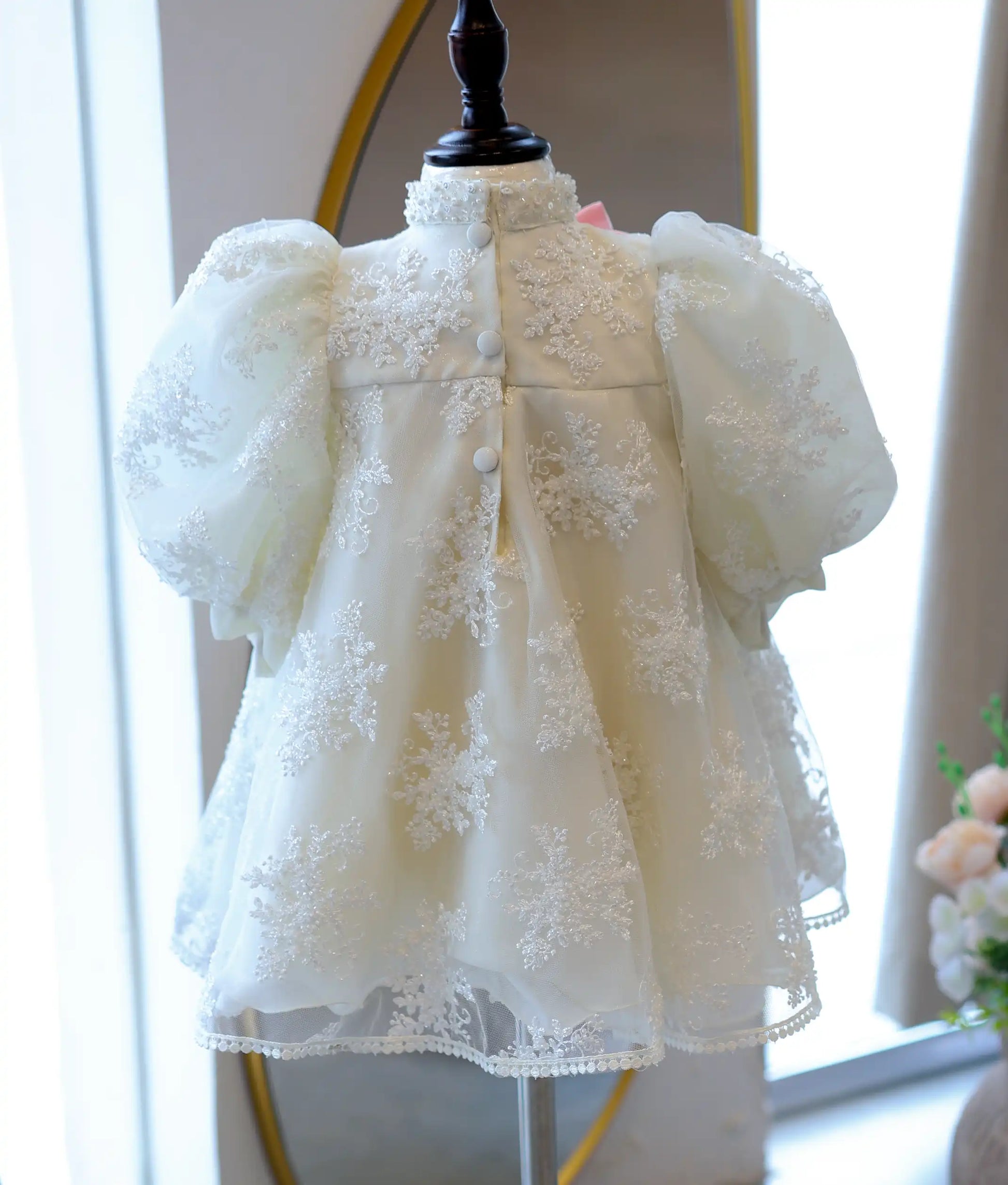 Detailed back view of the off-white kid's dress on a mannequin, displaying the high-neck design, embroidered net pattern, and clean fabric button closures.