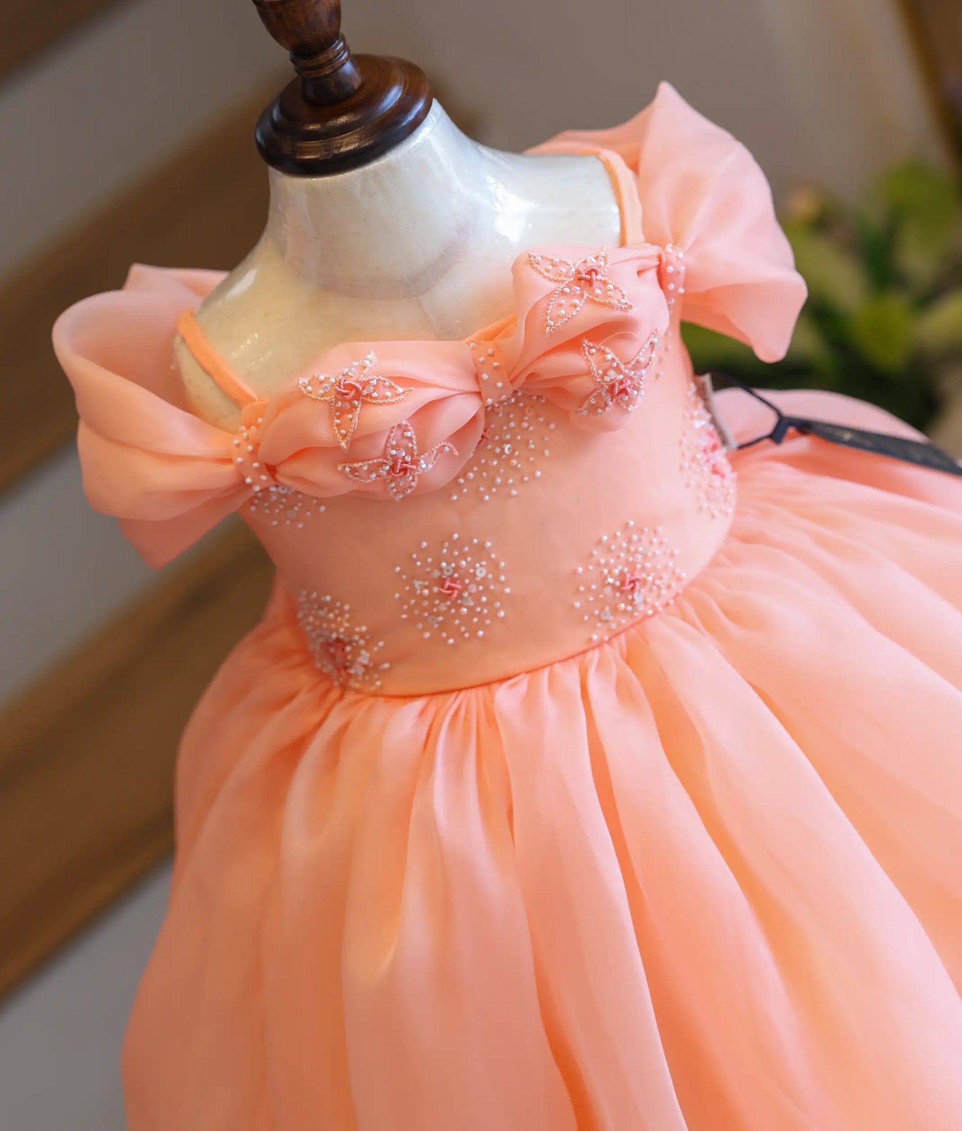 Close-up view of the dress top, highlighting the large pleated bow design embellished with white pearls and pink beaded flowers.
