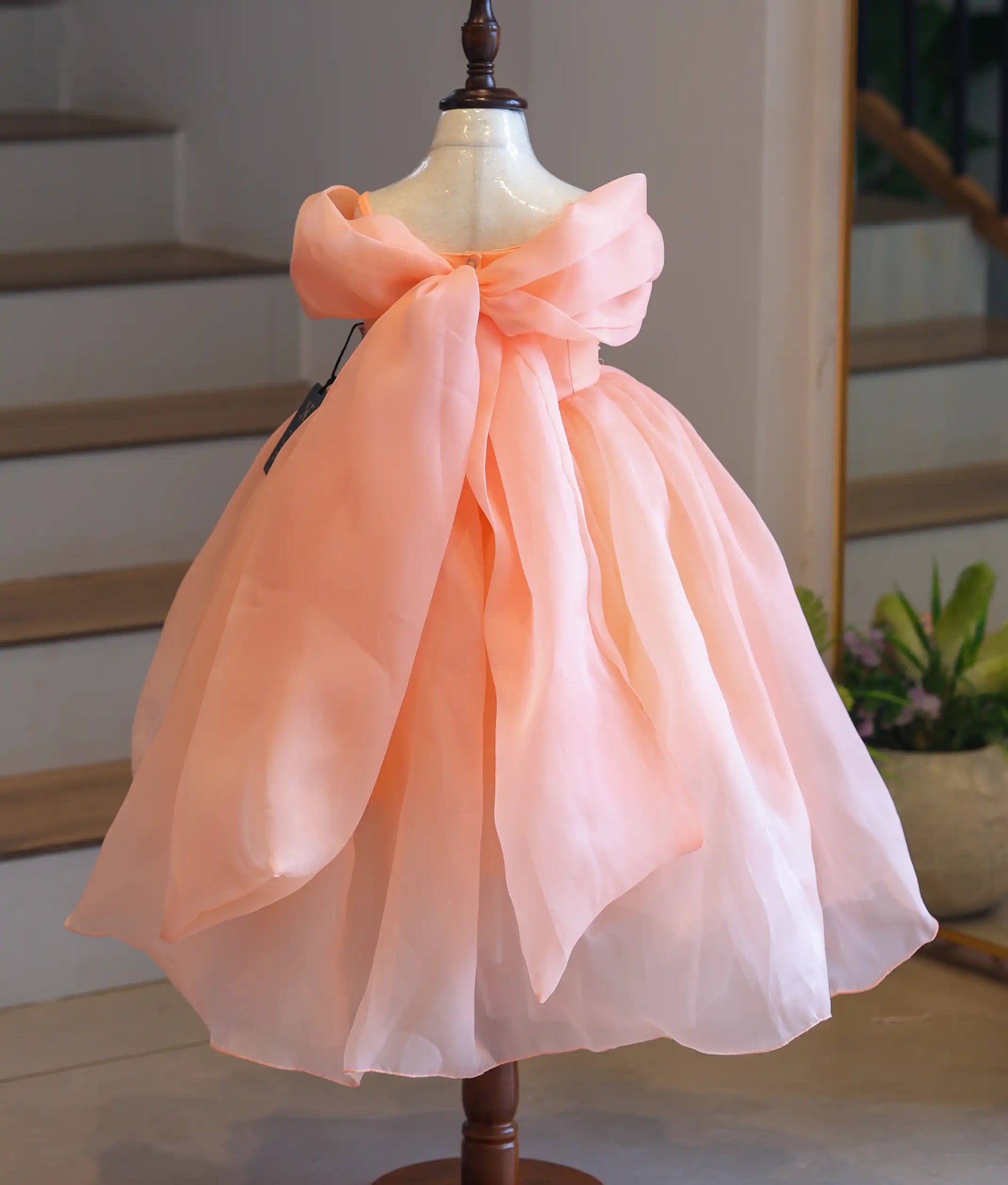 Back view of the kids' peach party gown on a mannequin, displaying the magnificent oversized organza back bow and trailing sashes.