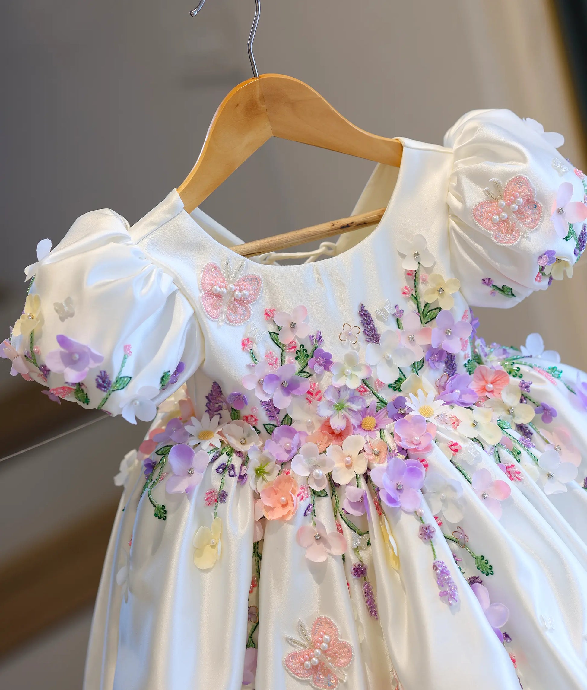 Close-up front view of the kids' dress bodice, showing the detailed 3D fabric flowers in lilac and peach, puff sleeves, and embroidered pink lace butterflies.
