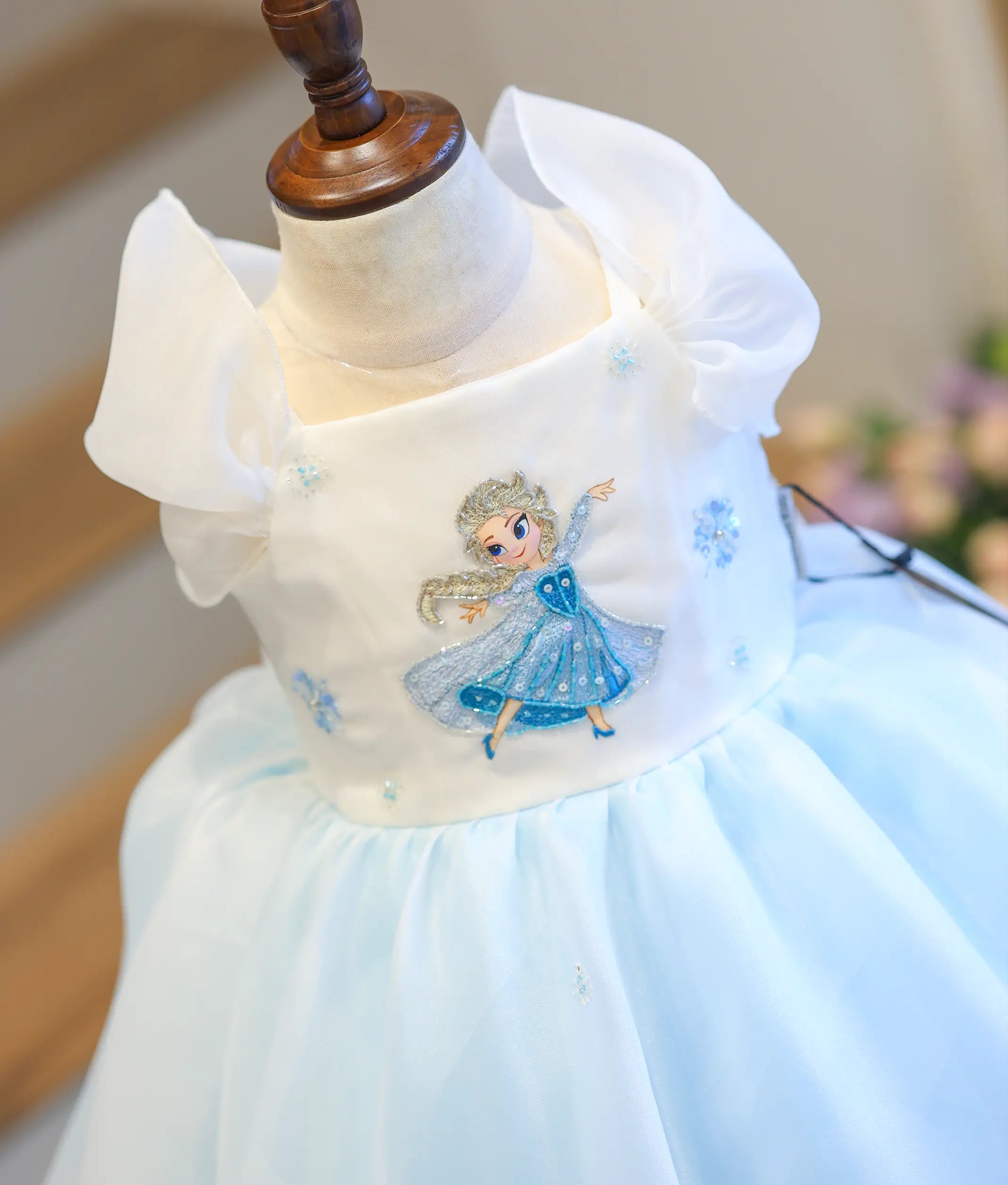 Detailed close-up view of the dress top, highlighting the hand-detailed Elsa patch, embroidered blue snowflakes, and soft white organza sleeves.
