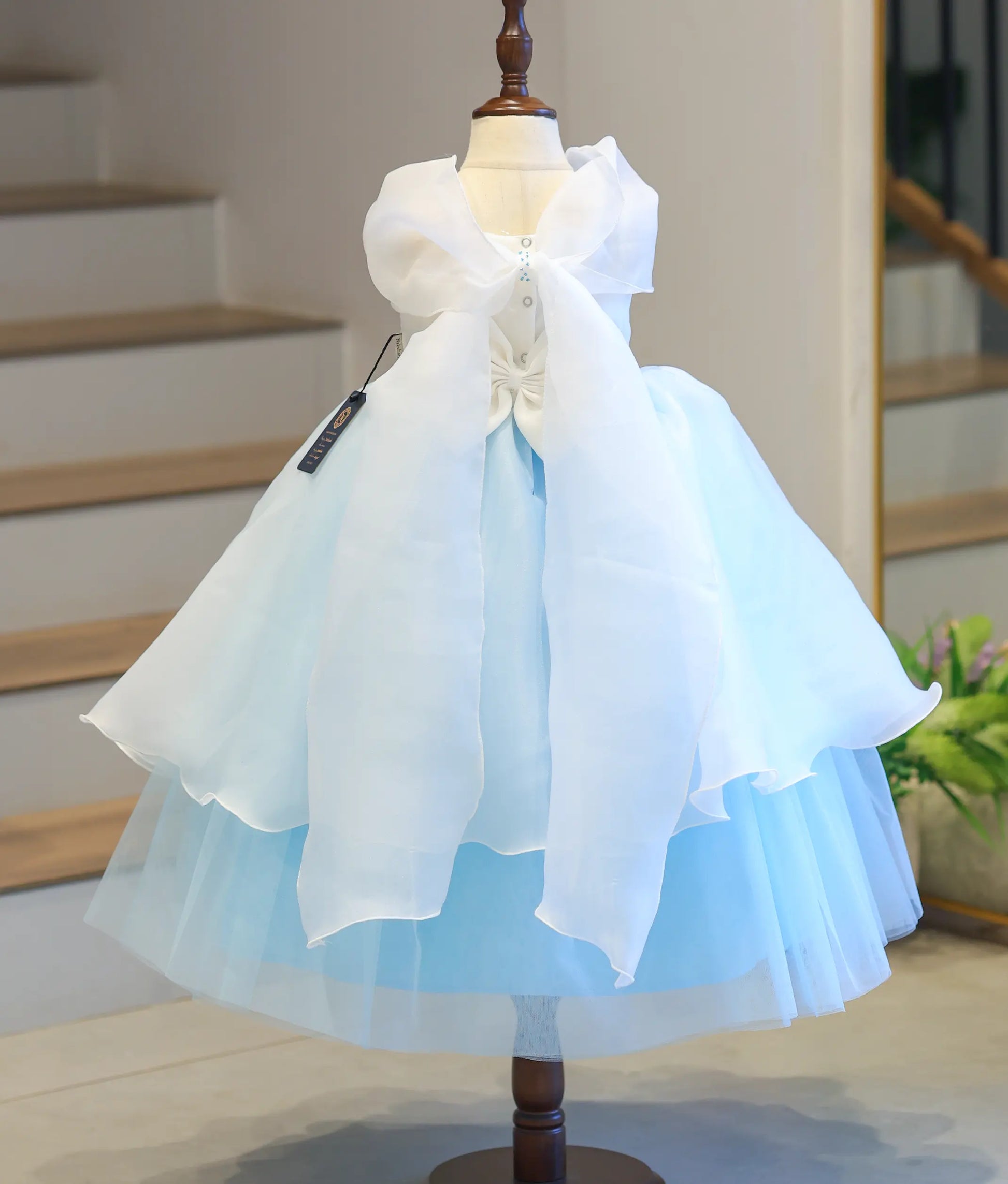 Full back view of the ice blue kid's princess dress on a mannequin, displaying the neat button closures and the dramatic white organza bow layout.