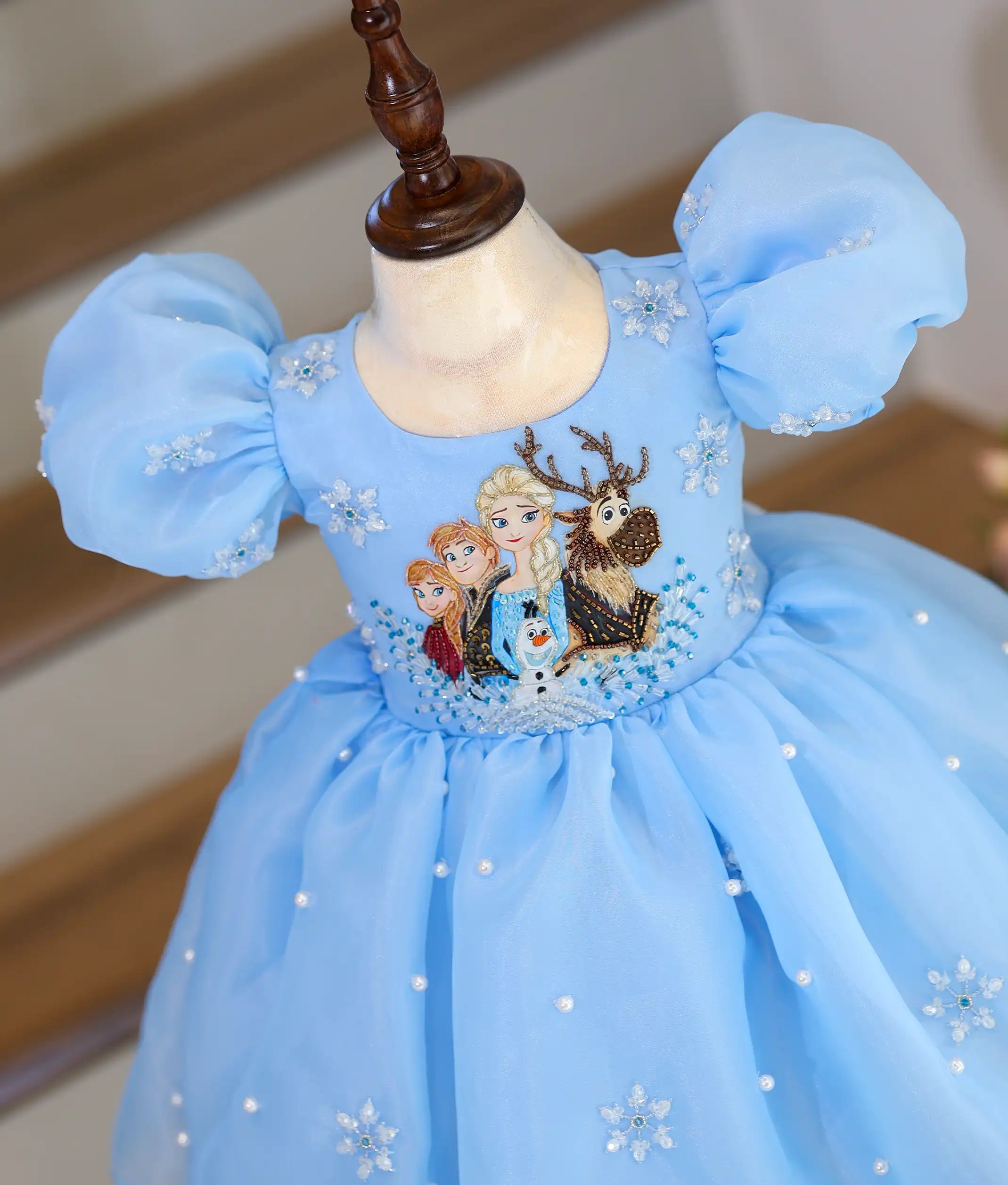 Angled view of a Frozen theme sky blue organza birthday dress for baby girl with handcrafted embroidery, puff sleeves, pearl embellishments, and flared skirt.