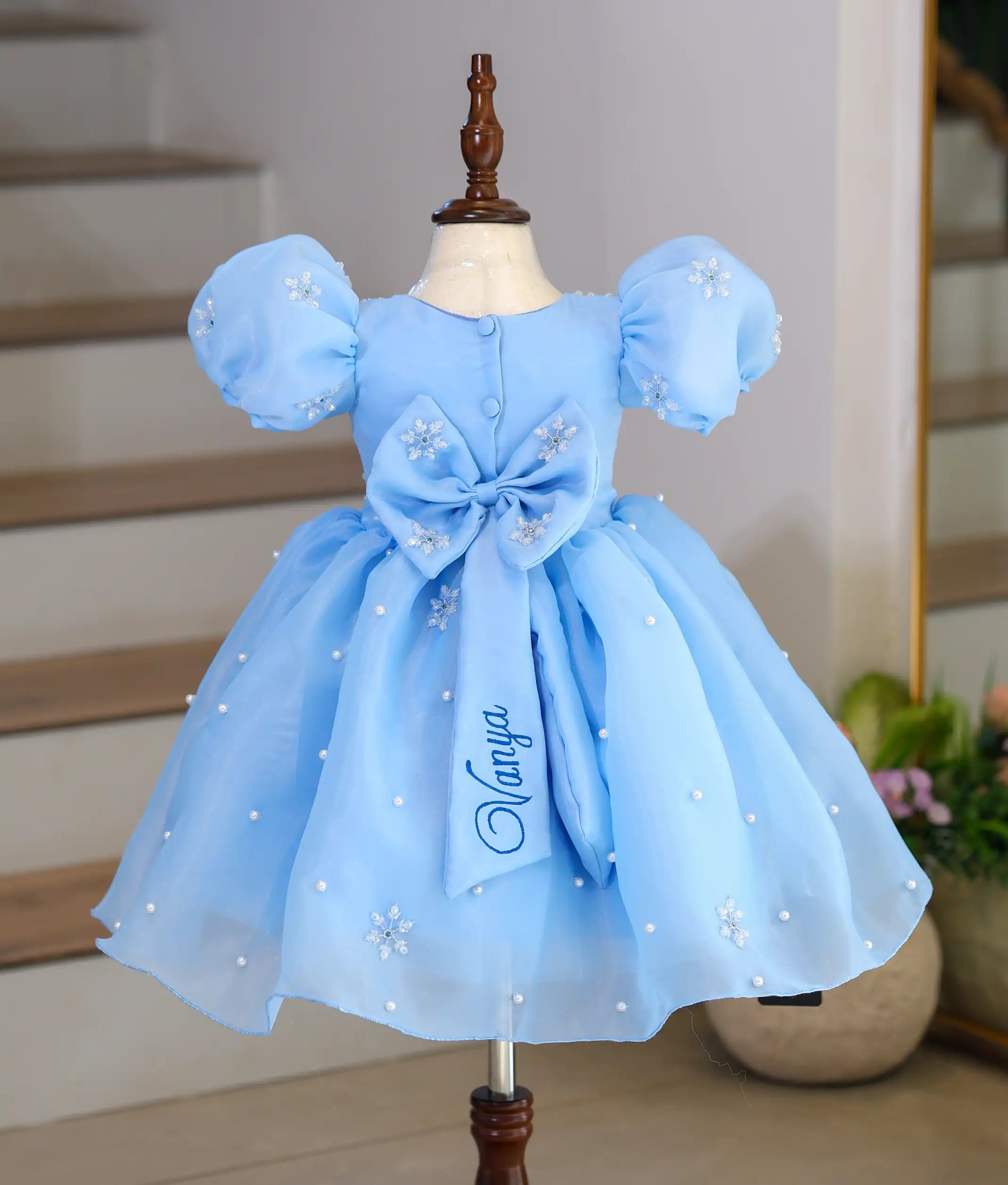 Back view of Frozen theme sky blue organza frock for baby girl featuring a statement bow, puff sleeves, pearl embellishments, and snowflake embroidery.