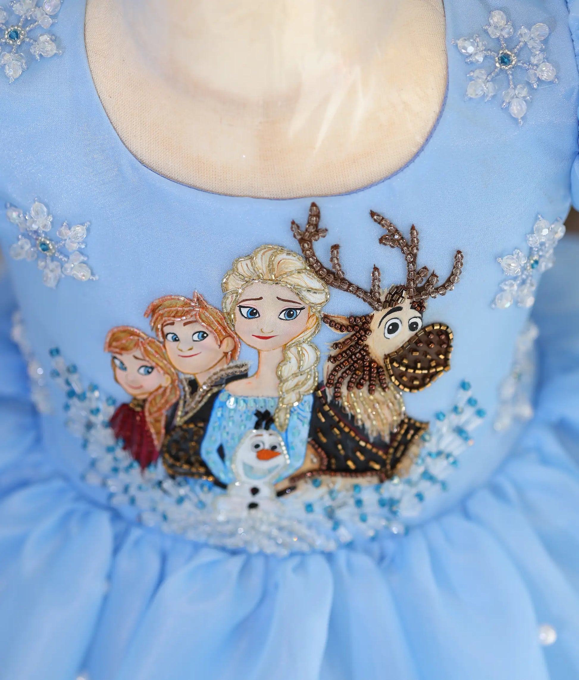 Close-up of Frozen-inspired hand embroidery with Elsa, Anna, Olaf, Sven, cut beads, sequins, and snowflake embellishments on a sky blue organza frock.
