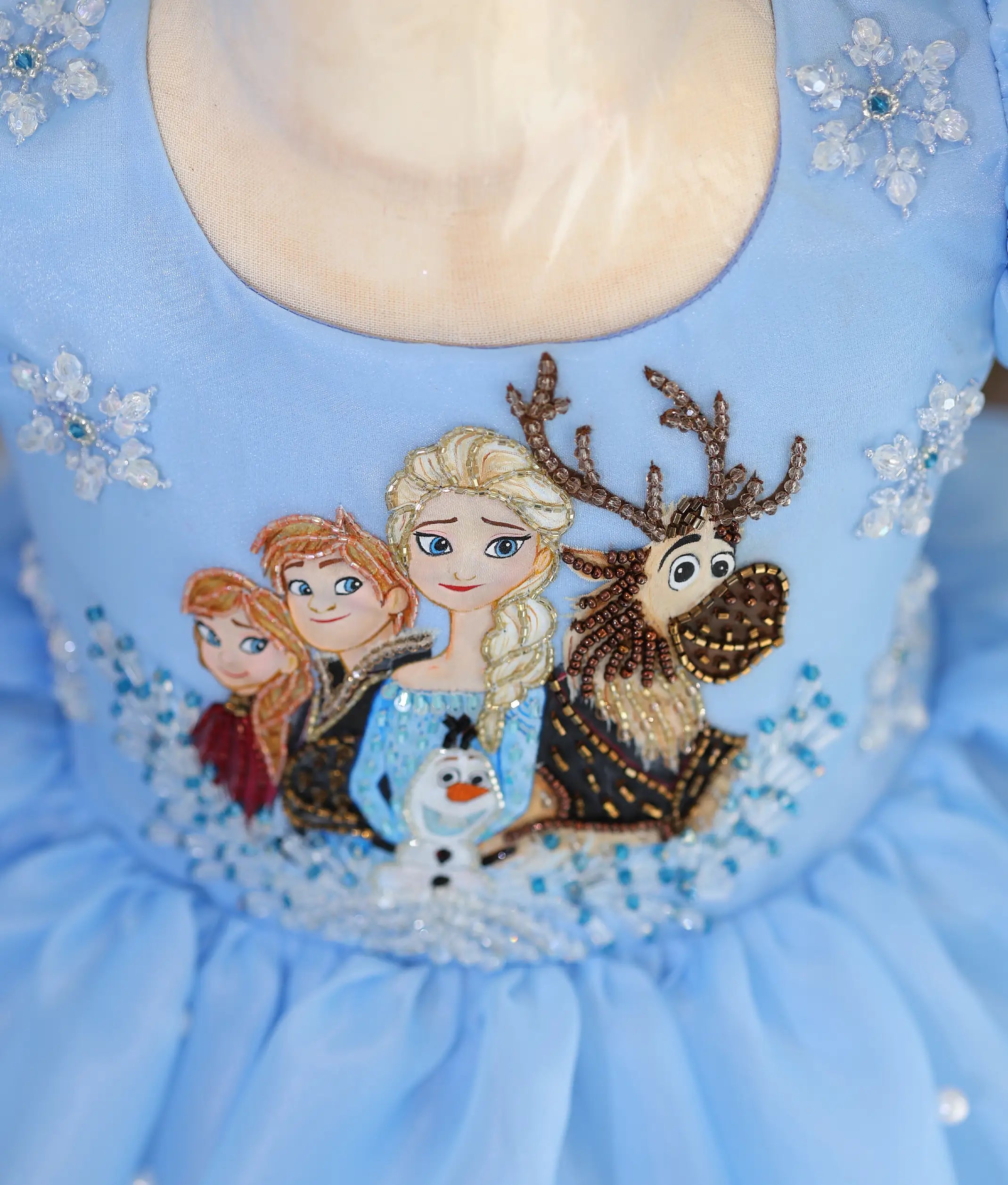 Close-up of Frozen-inspired hand embroidery with Elsa, Anna, Olaf, Sven, cut beads, sequins, and snowflake embellishments on a sky blue organza frock.