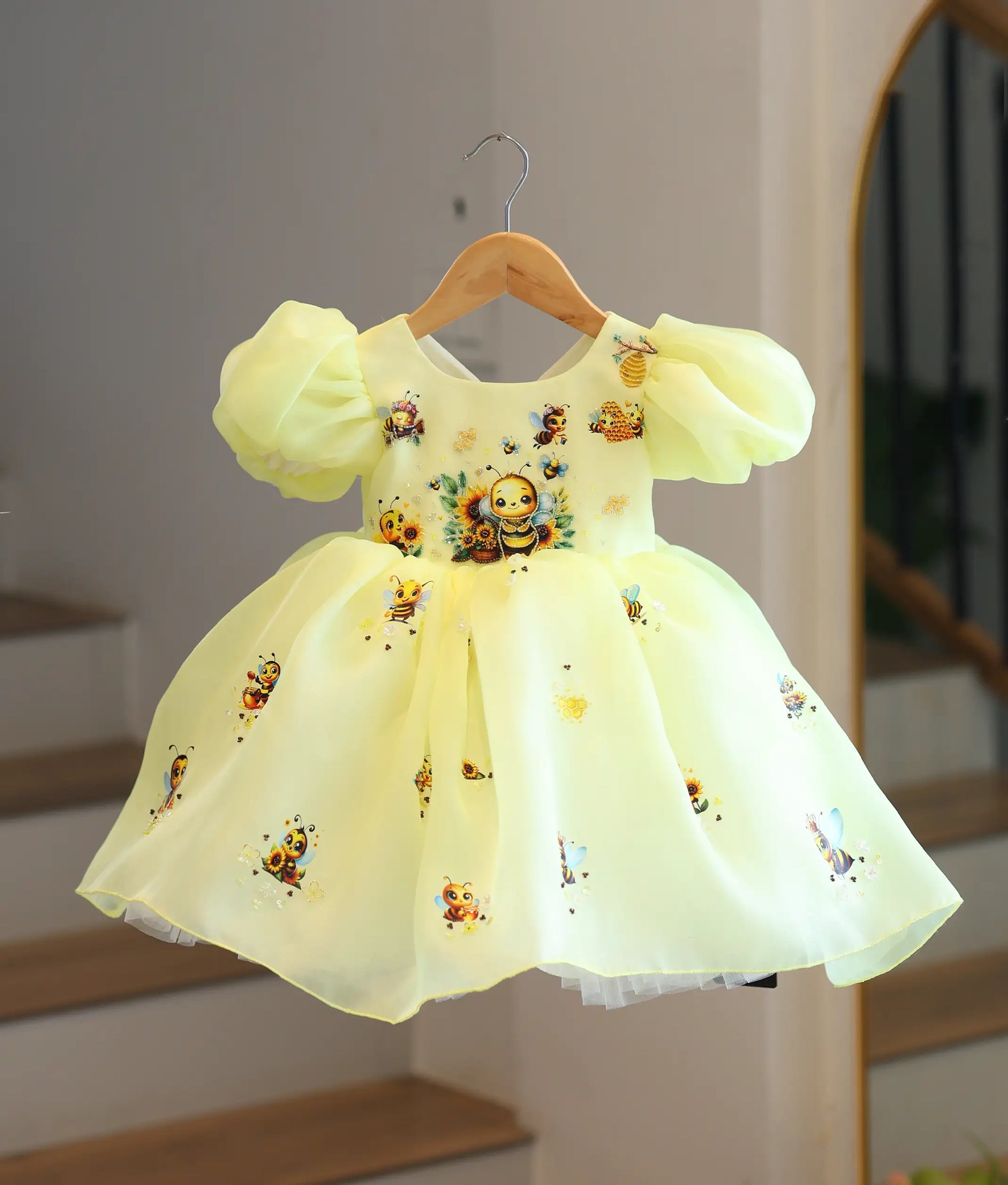 Full front view of a premium kids' lemon yellow organza honeybee-themed party frock on a hanger, showing the sunflower details and full-flared skirt.