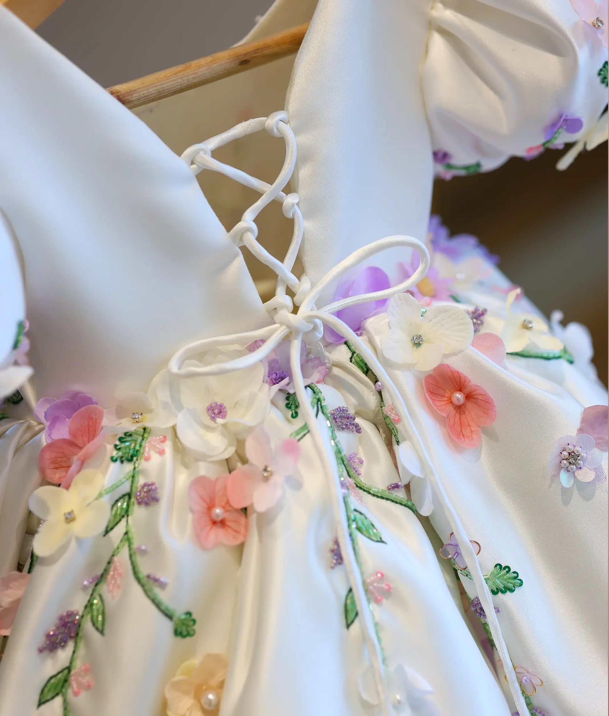 Close-up view of the back of the dress, highlighting the white satin corset tie-up system, embroidered flower borders, and scattered beads.