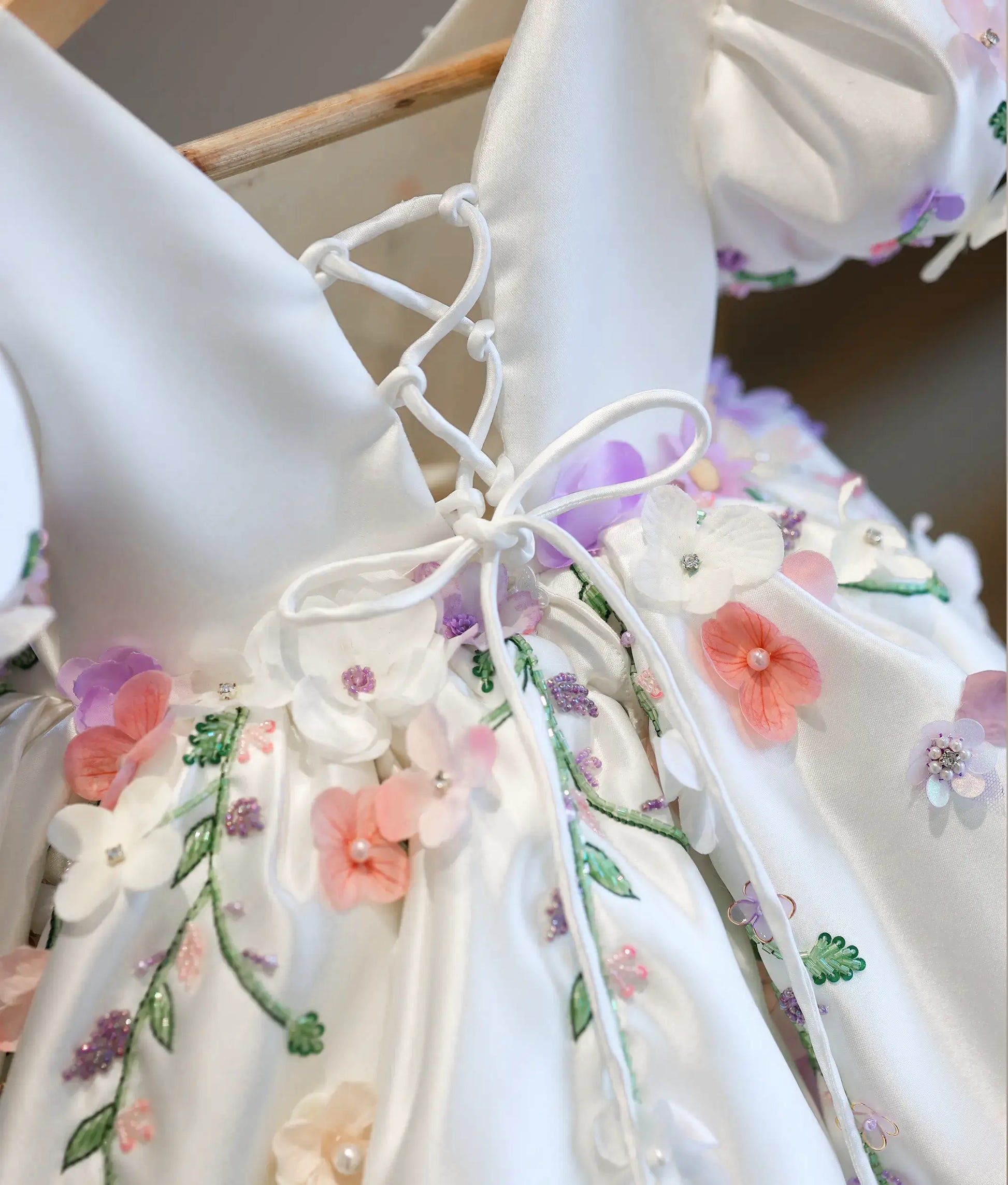Close-up view of the back of the dress, highlighting the white satin corset tie-up system, embroidered flower borders, and scattered beads.
