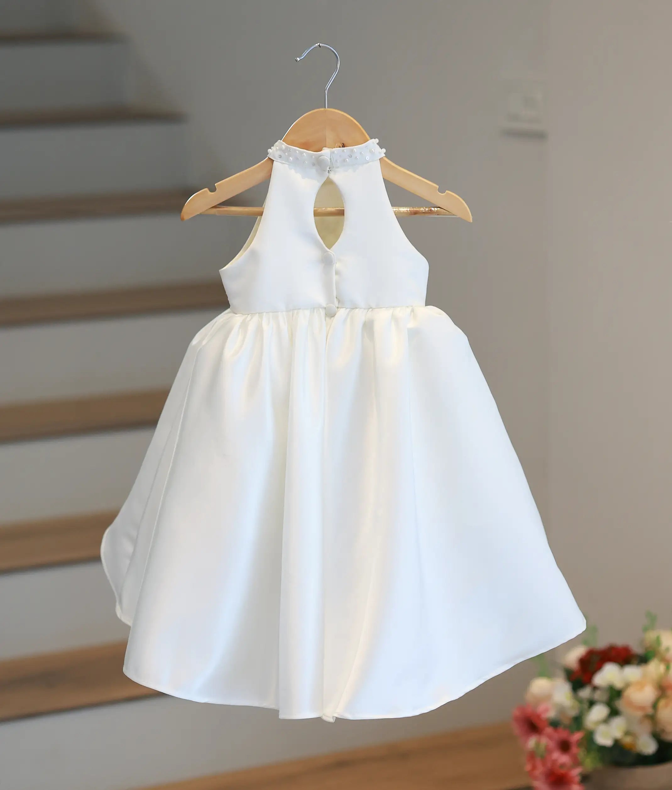 Back view of the off-white kid's party gown on a hanger, displaying the elegant teardrop keyhole back design and fabric button closures.