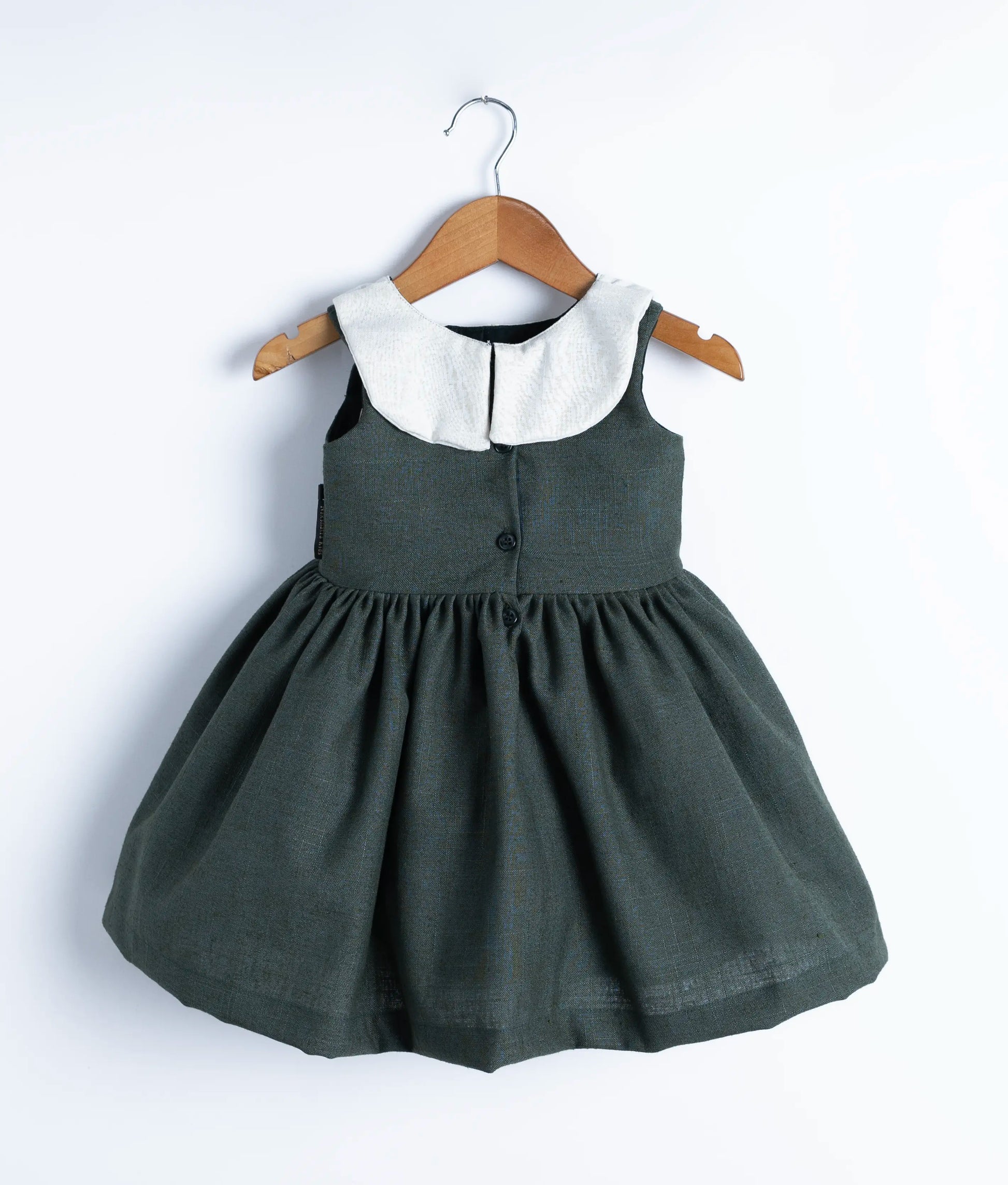 Back view of the knee-length green linen dress, highlighting the pleated, gathered skirt and round neck button closure.
