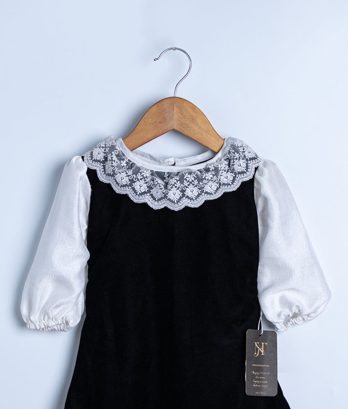 Close-up of the delicate white lace trim detail around the round neckline on the black velvet party dress.