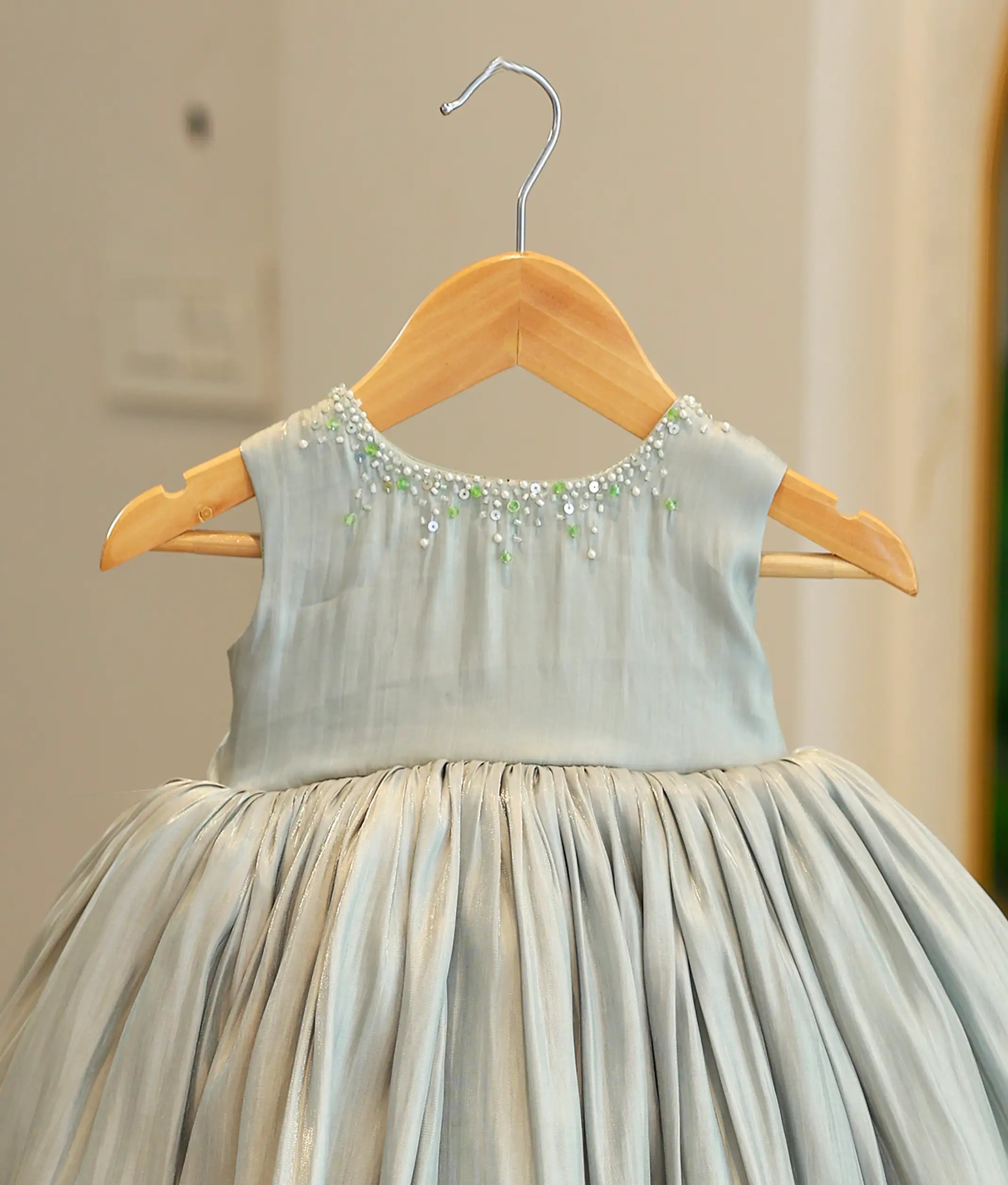 Detailed view of the green frock's bodice highlighting the transparent round neck with scattered pearls and the horizontal floral embroidery band at the waistline.