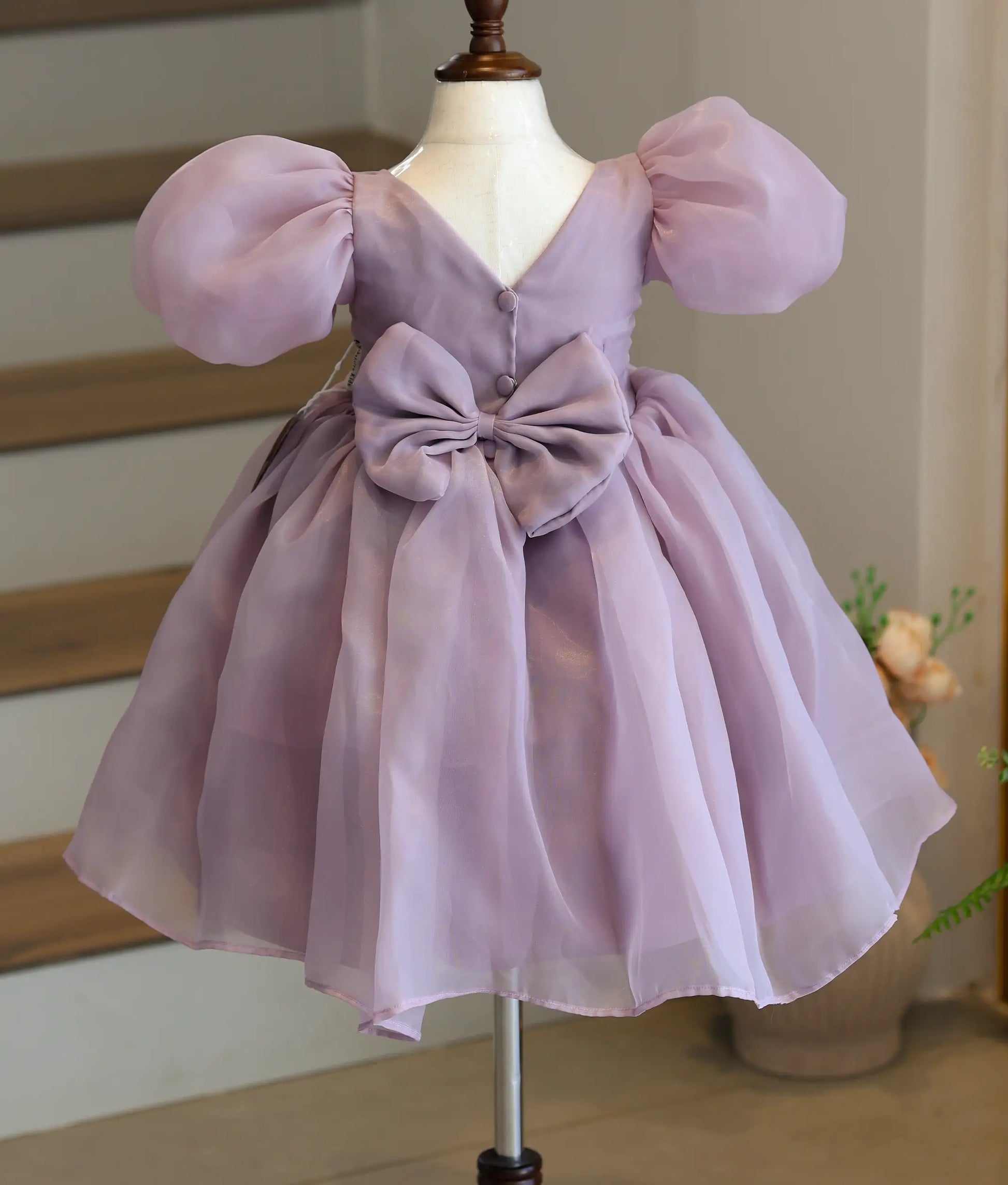 Back view of the lavender frock showing the elegant V-neck lace design and a large decorative bow