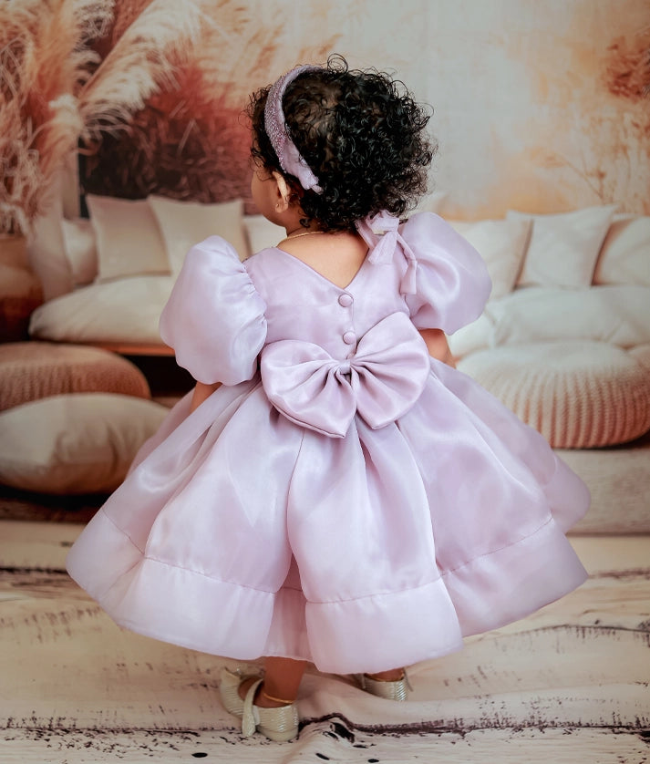 Back view of a lavender frock showing the V-neck design, show button, and large decorative organza bow