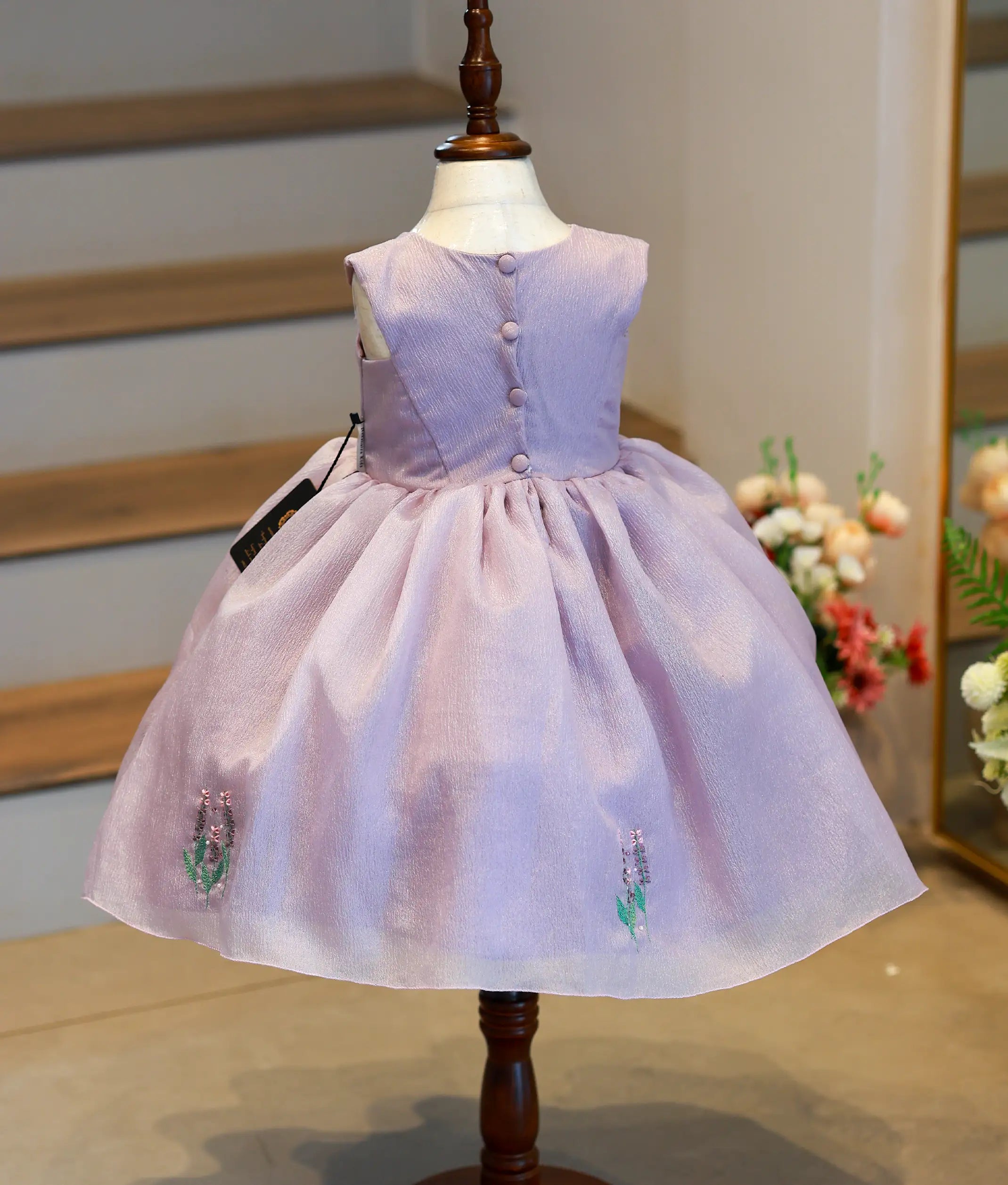 Back view of lavender crush organza frock showing the round neckline with show button and the full gathered skirt