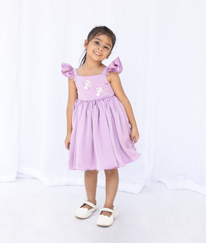 Close-up of the pastel lavender dress bodice showing the handworked unicorn embroidery and square neckline
