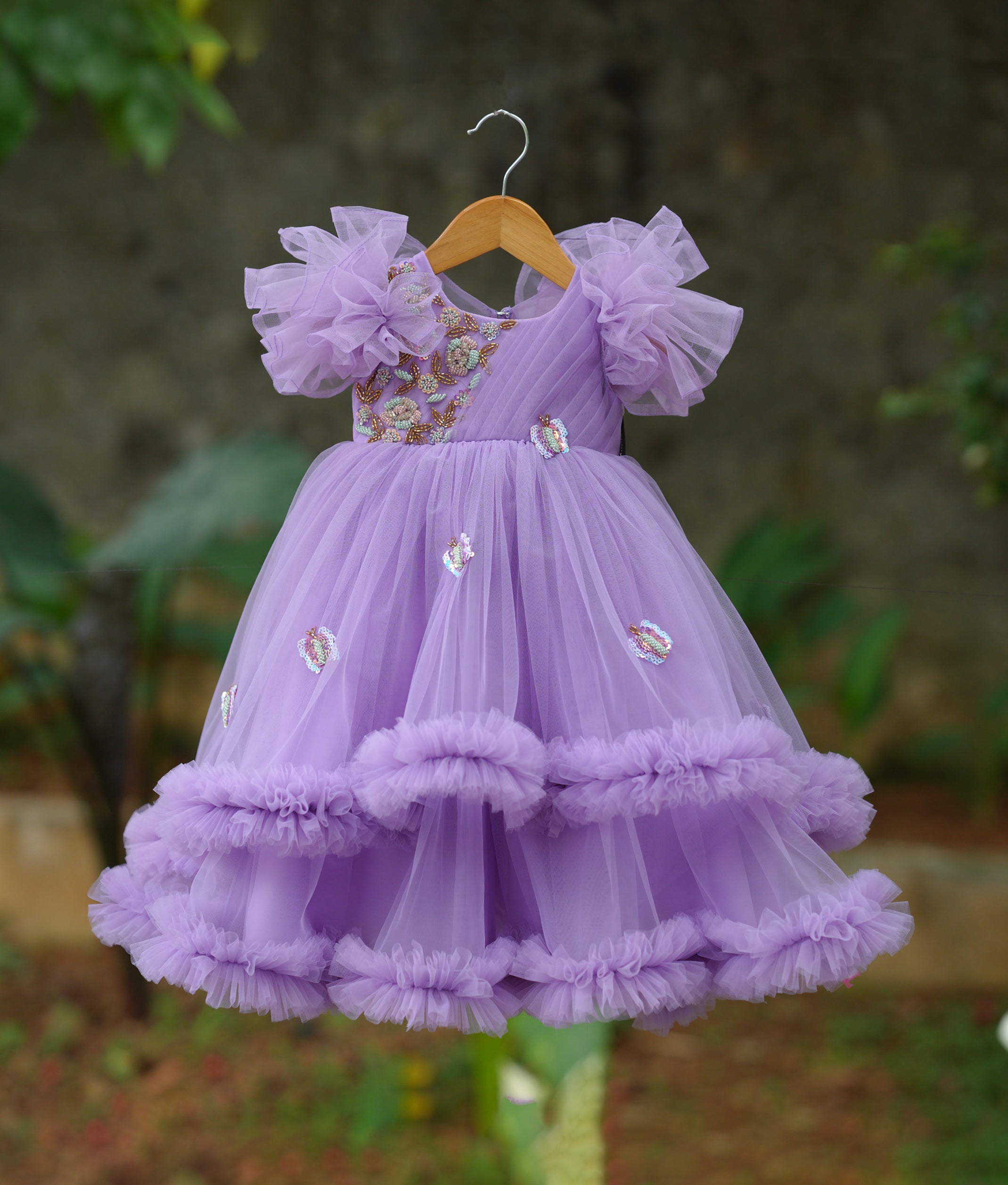 Front view of a lavender butterfly theme birthday gown with floral handwork and a voluminous frilled skirt