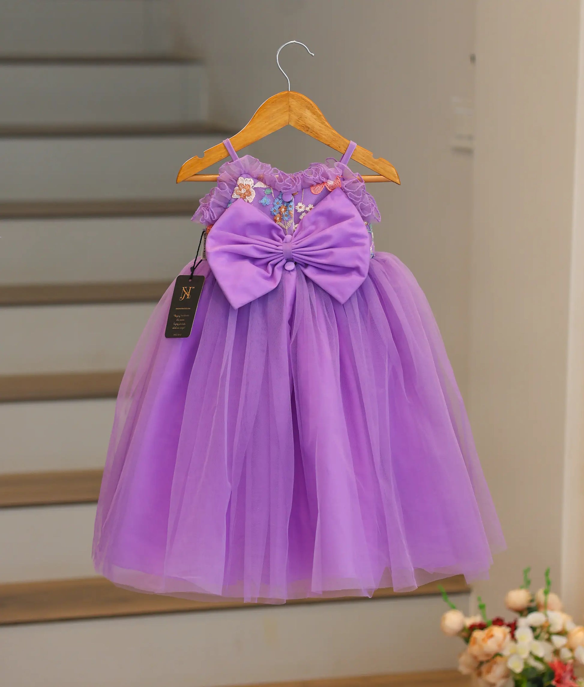 Back view of the lavender organza frock showing the round neck, button closure, and decorative bow with tie