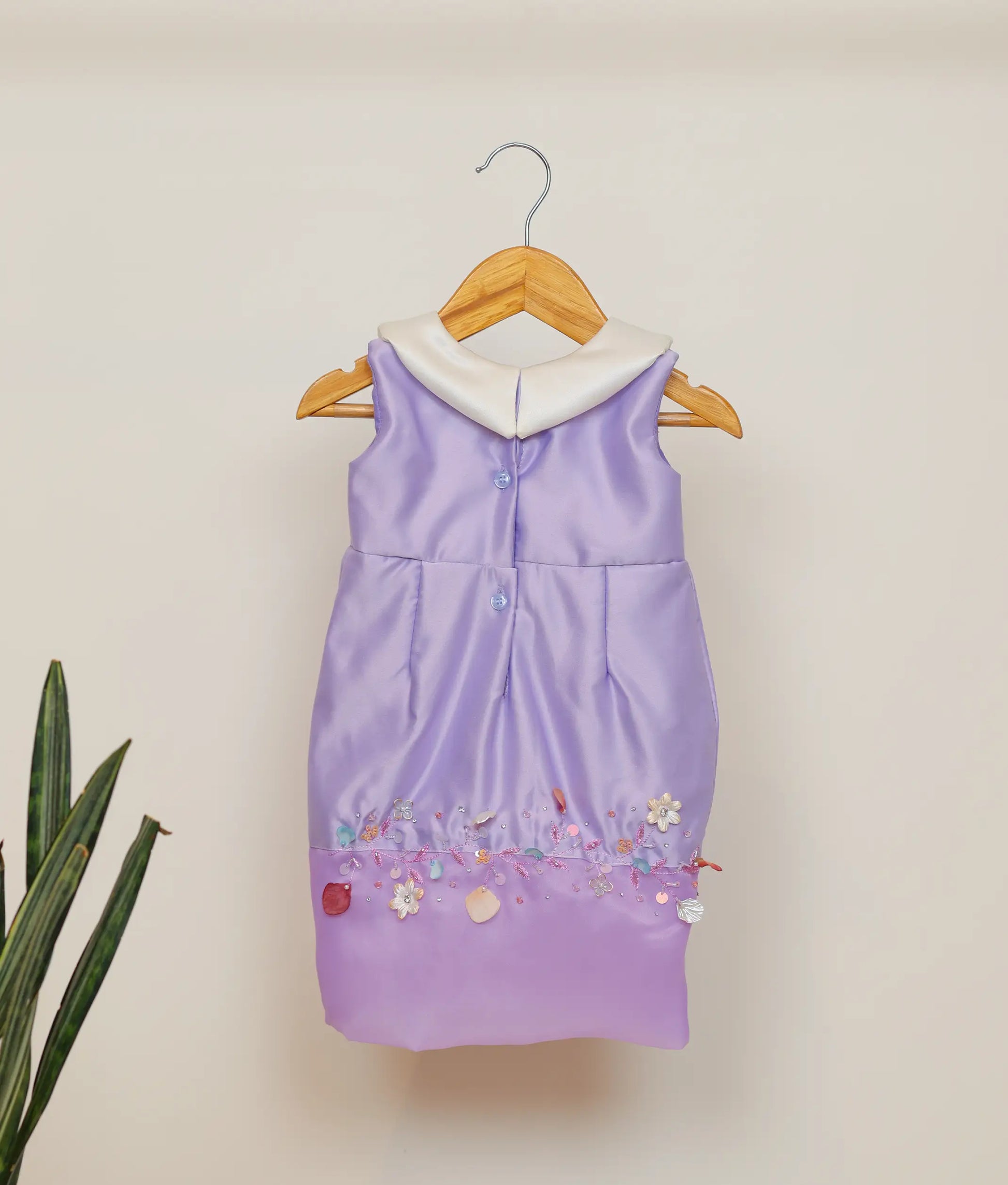 Back view of lavender satin fish-cut frock showing the round neckline with button closure and the elegant flow of the below-knee skirt