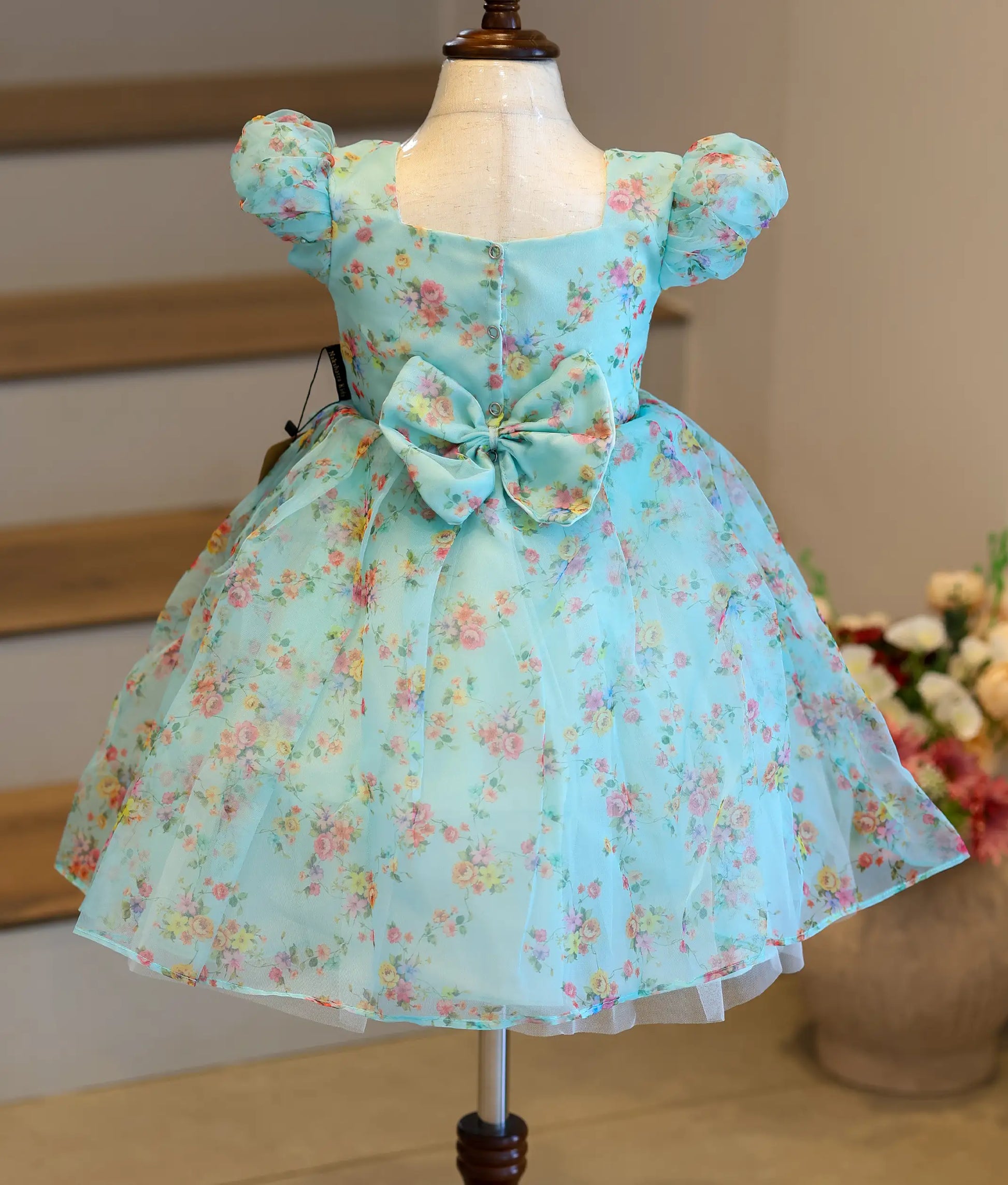 Back view of the light blue printed organza frock showing the square neck, press button closure, and decorative bow