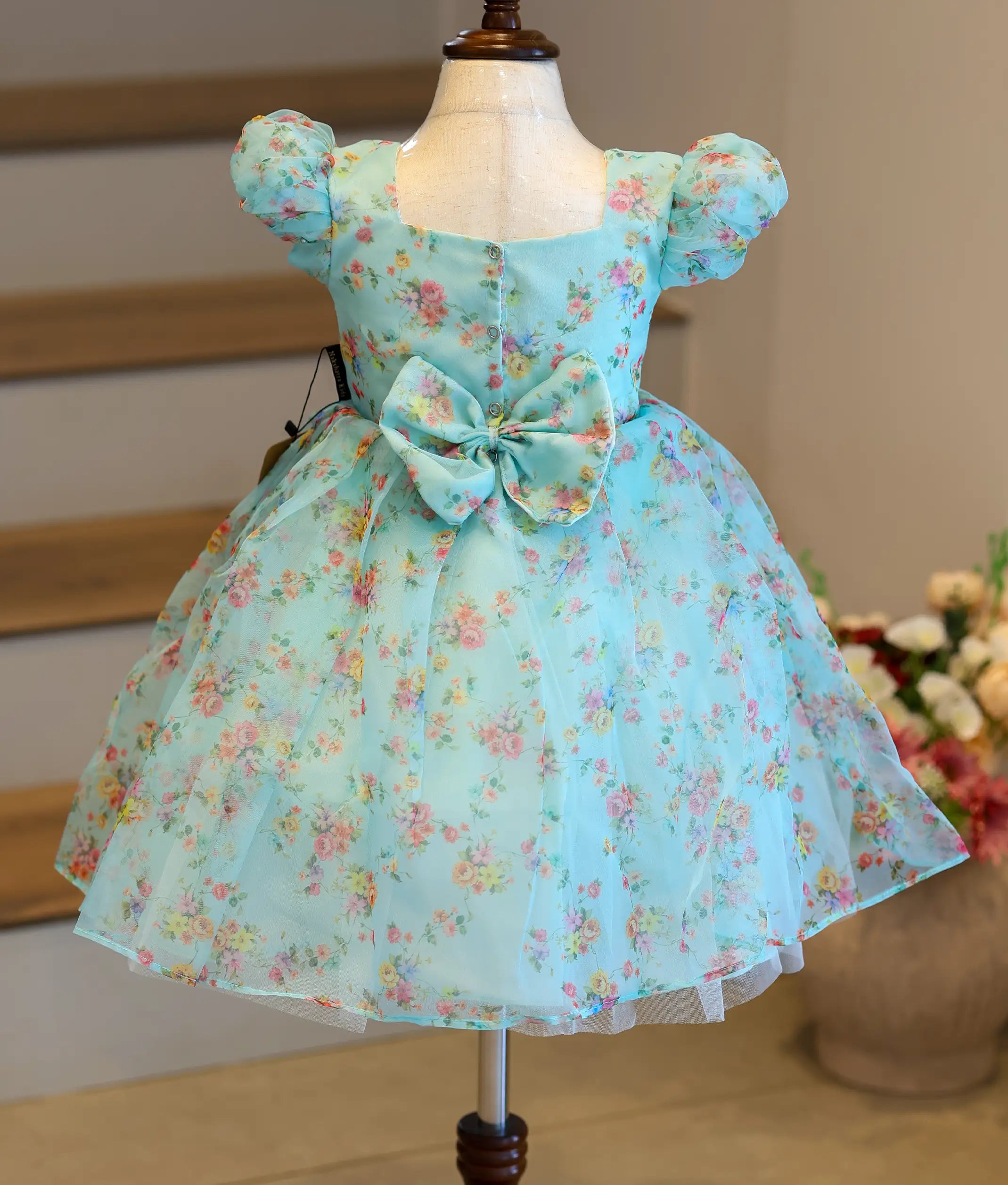 Back view of the light blue printed organza frock showing the square neck, press button closure, and decorative bow