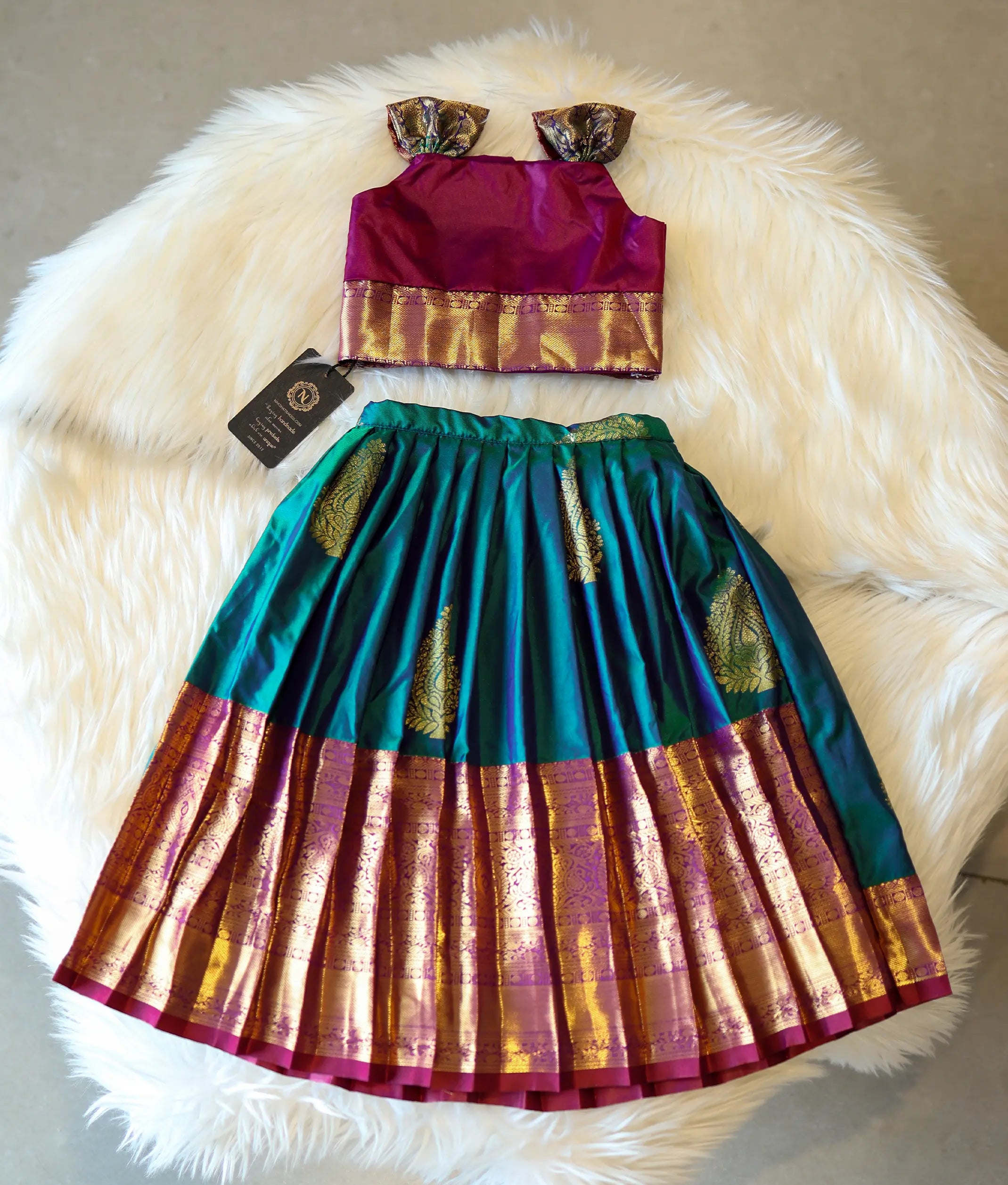 Front view of a magenta and peacock green Kanchipuram silk skirt and top for girls.