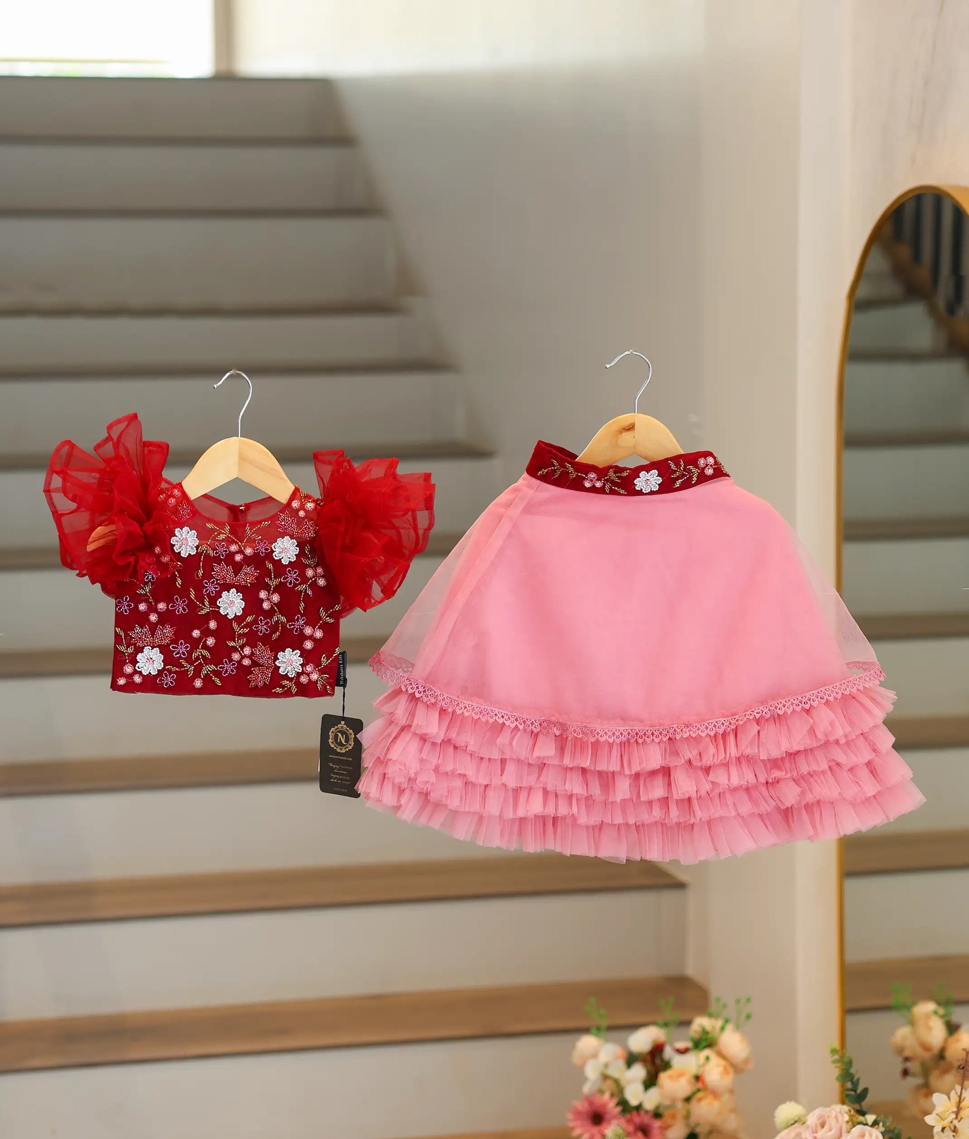 Front view of a baby girl outfit featuring a maroon handworked crop top and a tiered onion pink net skirt
