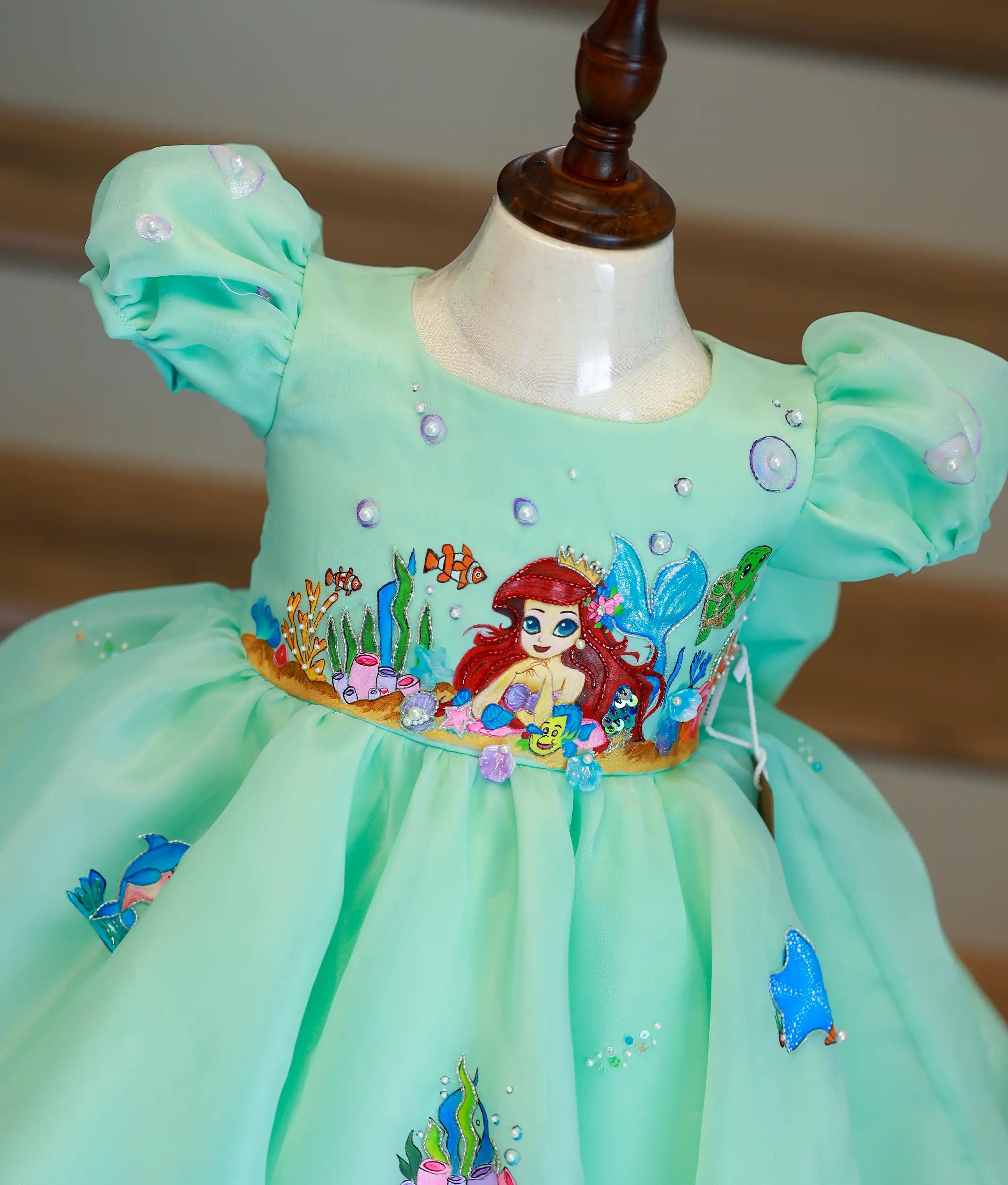 Close-up of the hand-painted mermaid, coral, and fish details on the sea green organza birthday gown