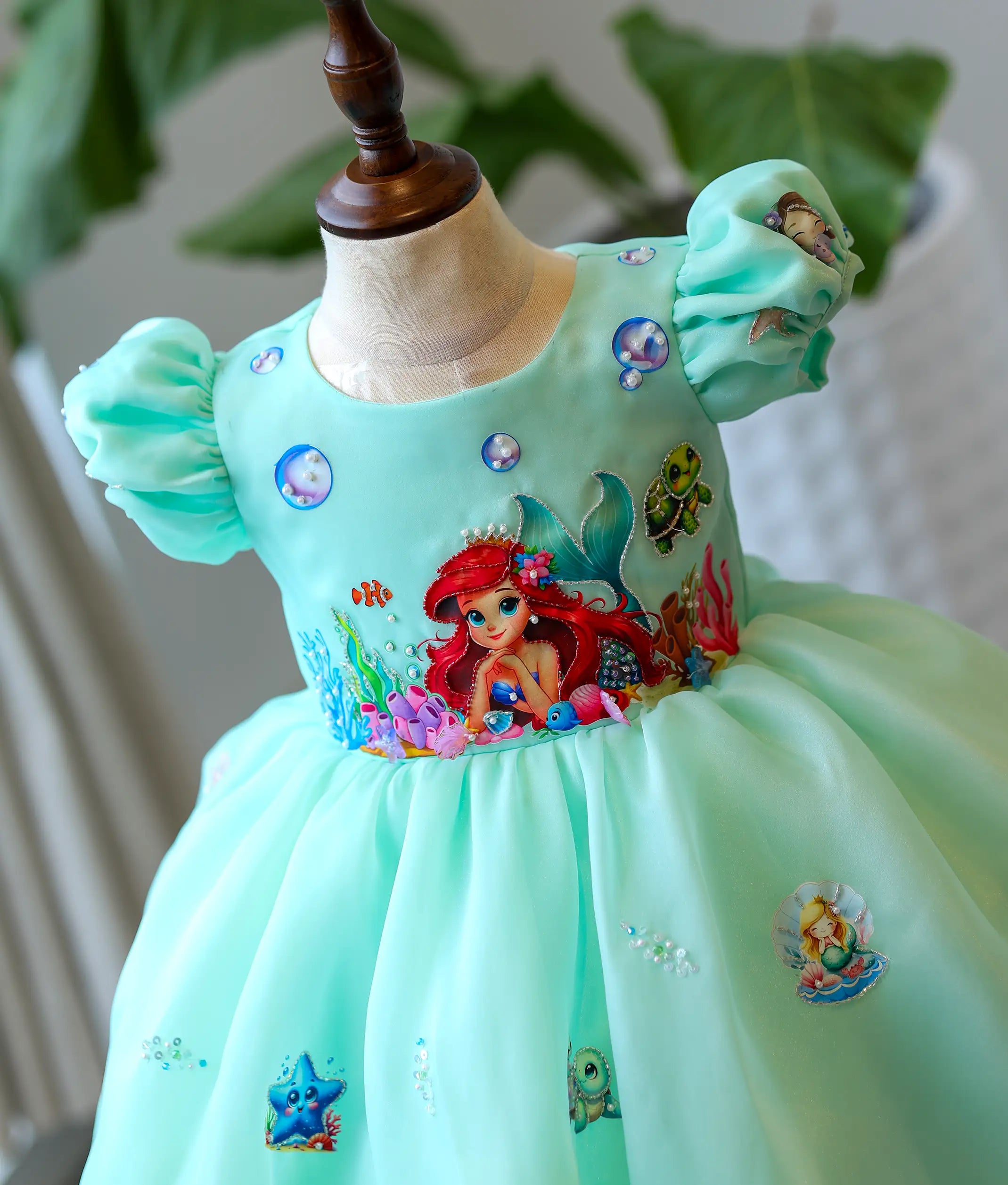 Close-up of the hand-painted mermaid, coral, and fish details on the sea green organza birthday gown