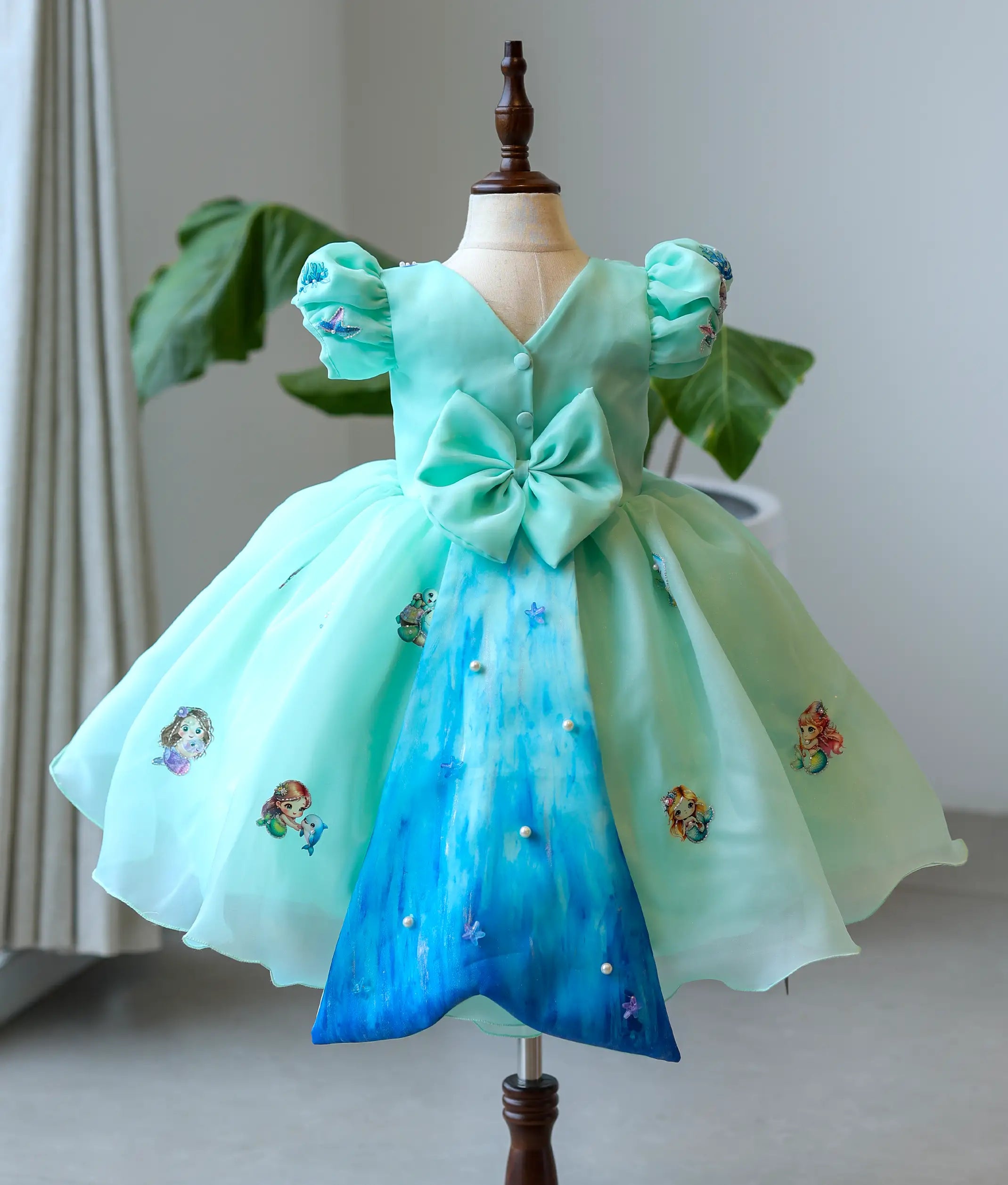 Back view of the mermaid theme frock showing the V-neck, decorative bow, and long wide mermaid-tail panel