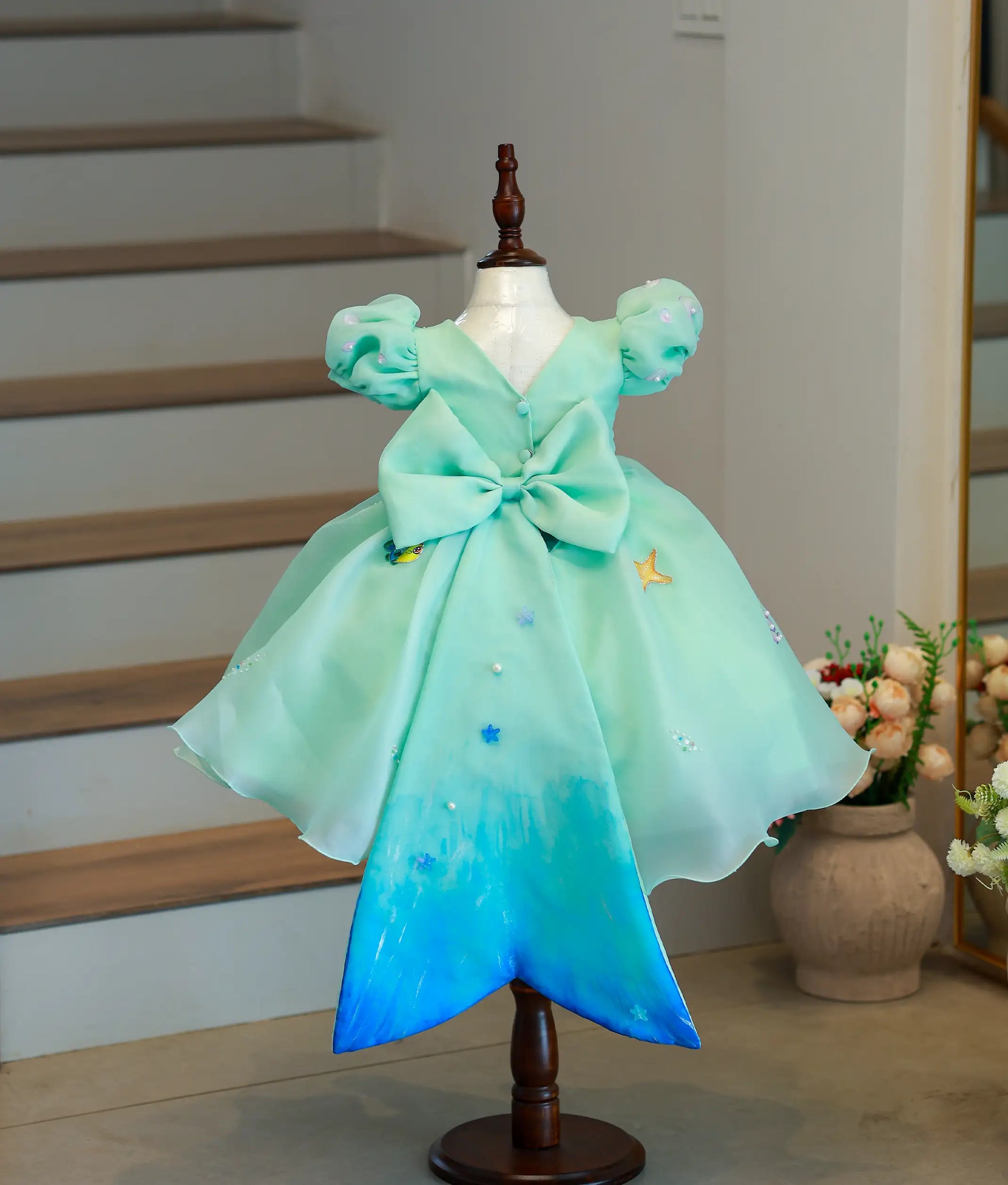 Back view of the mermaid theme gown showing the V-neck, decorative bow, and long wide mermaid-tail panel
