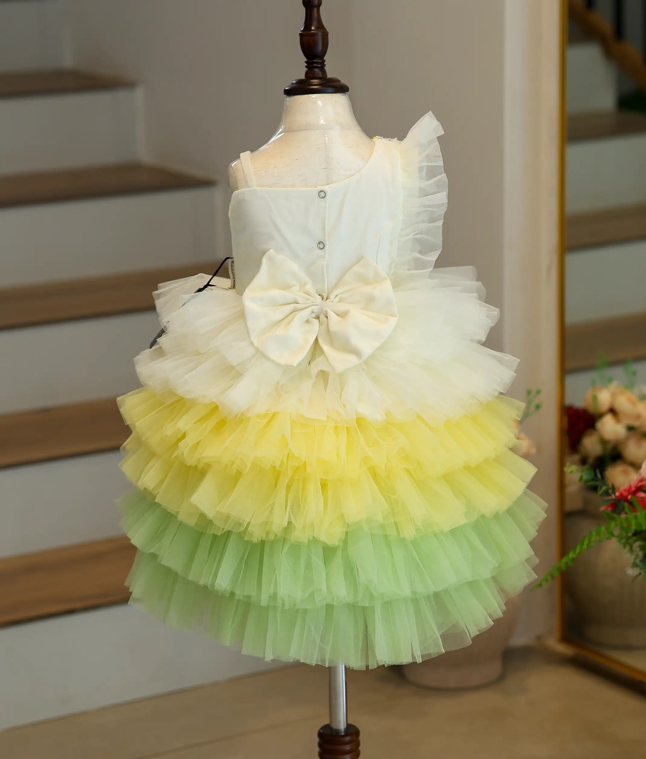Back view of a multi-color butterfly-themed birthday frock showing the bow detailing, snap button closure, and layered tulle net back.