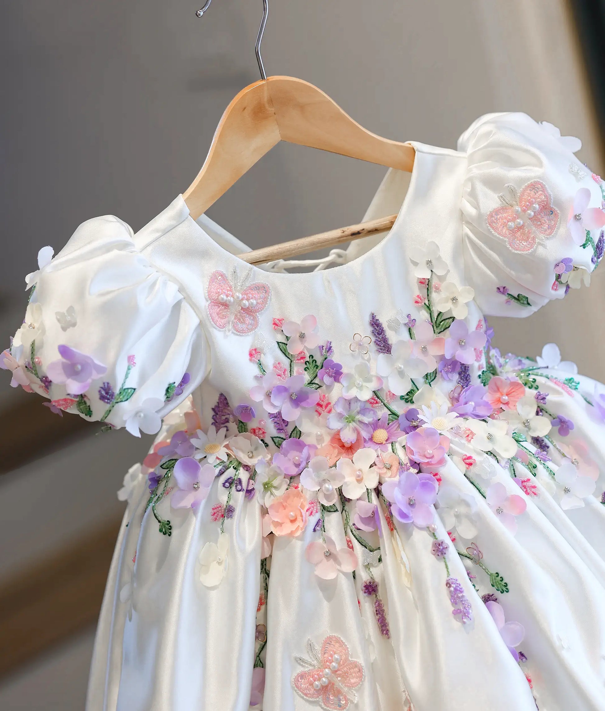 Close-up front view of the kids' dress bodice, showing the detailed 3D fabric flowers in lilac and peach, puff sleeves, and embroidered pink lace butterflies.