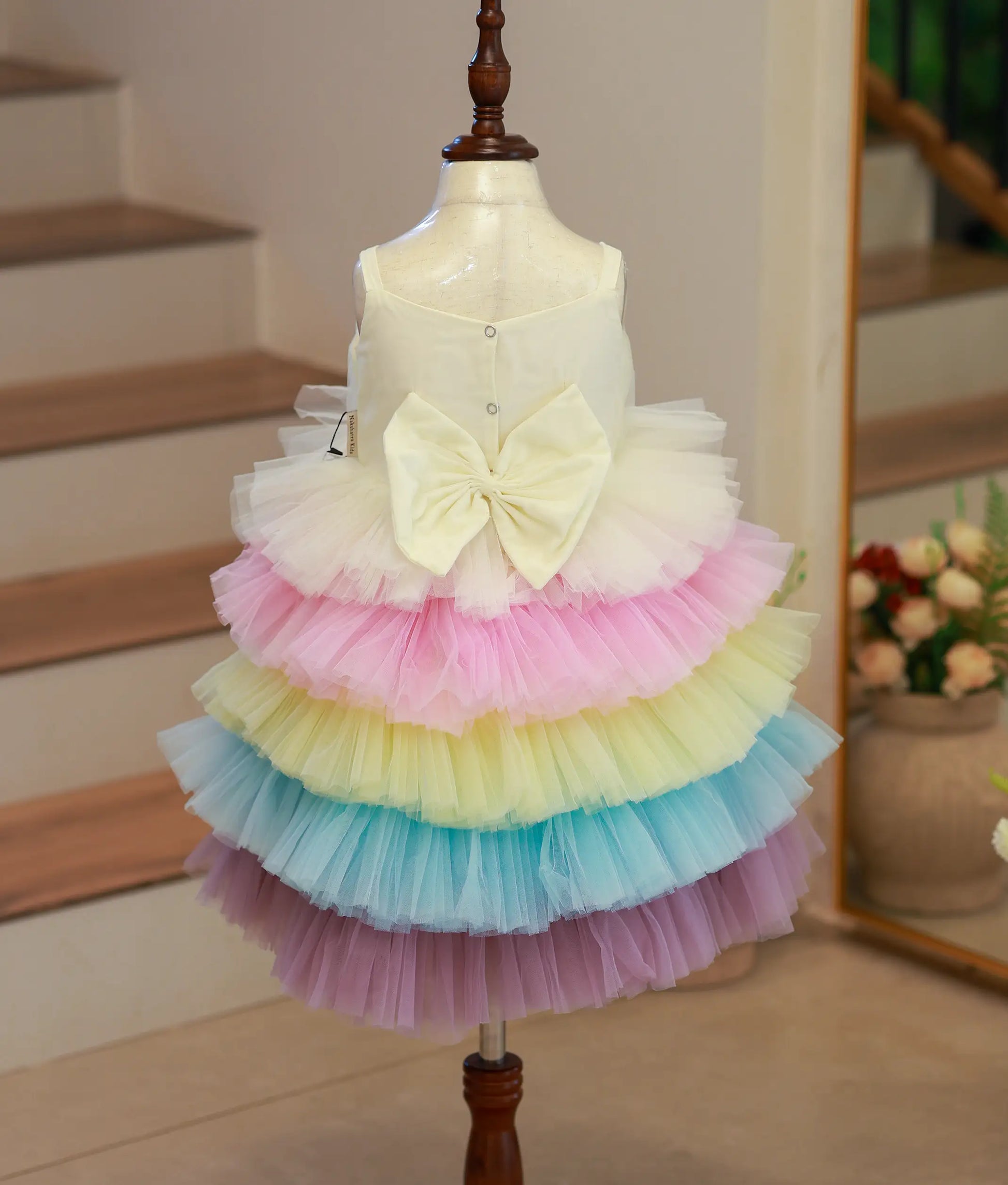 Back view of the multicolored birthday frock showing the square neck, press buttons, and decorative bow.